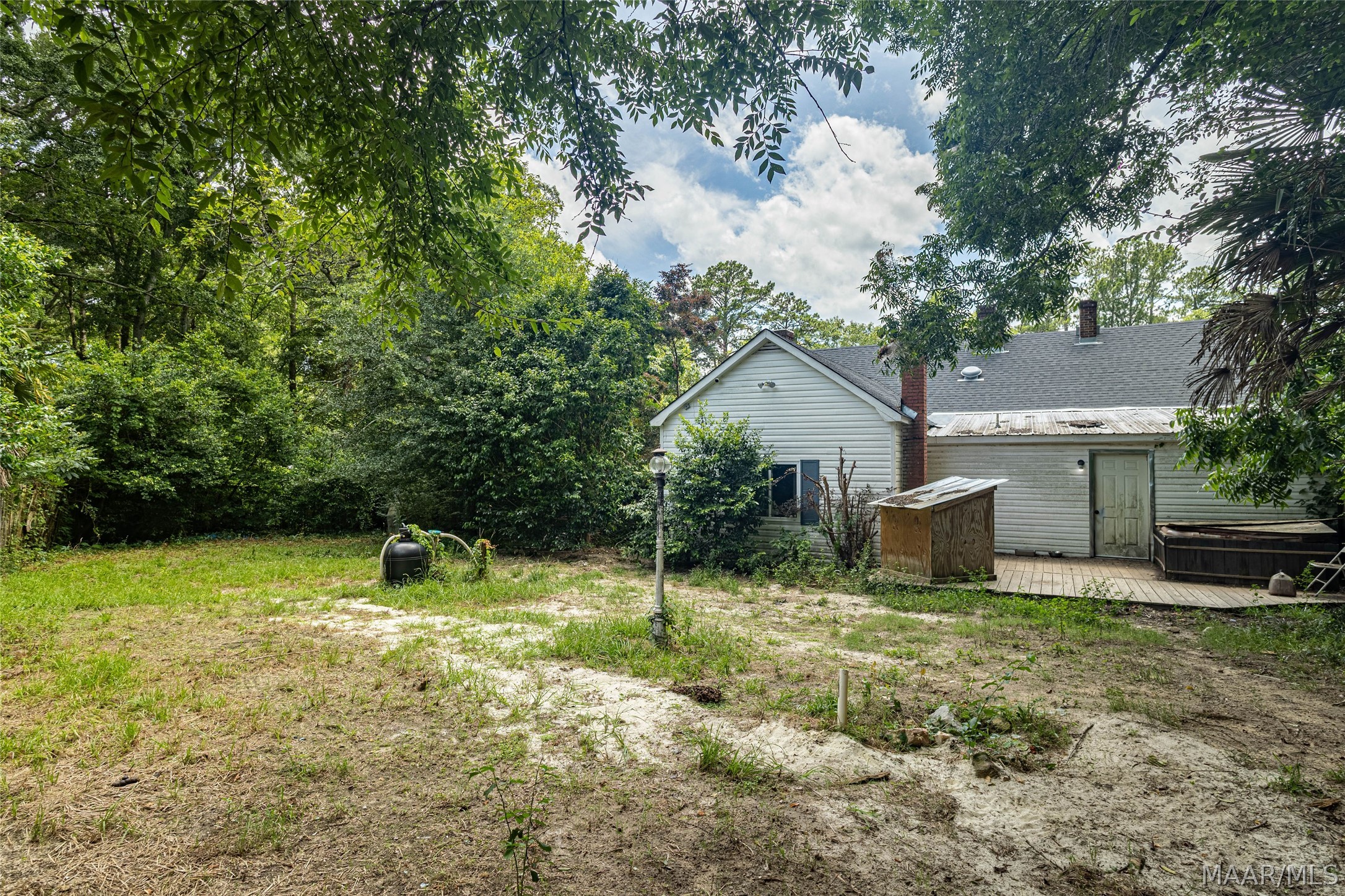 Rear of a light-colored house beside a wooded yard, deck, and outdoor hot tub.