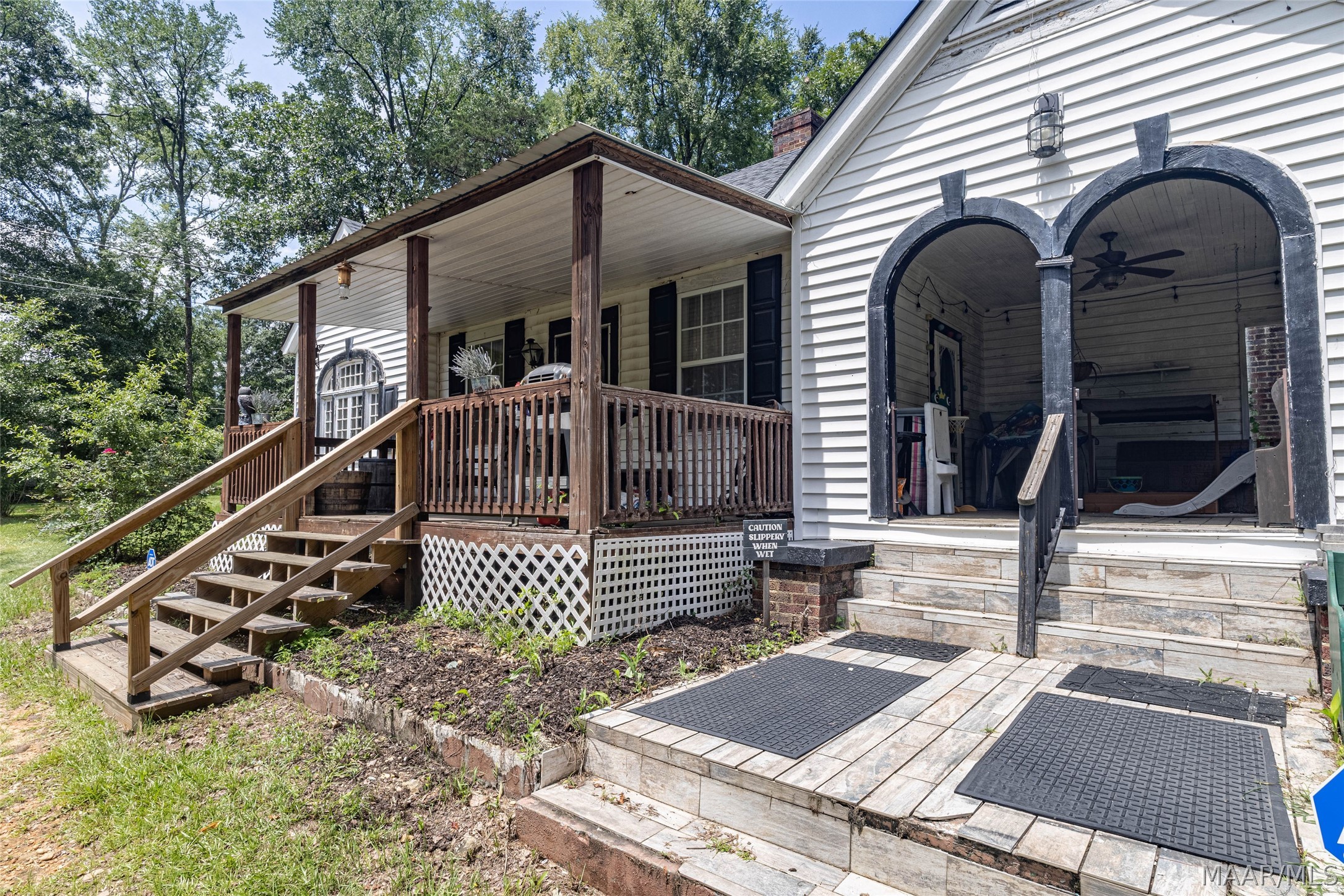 House exterior with a raised wooden porch beside a covered patio with dark arched openings.
