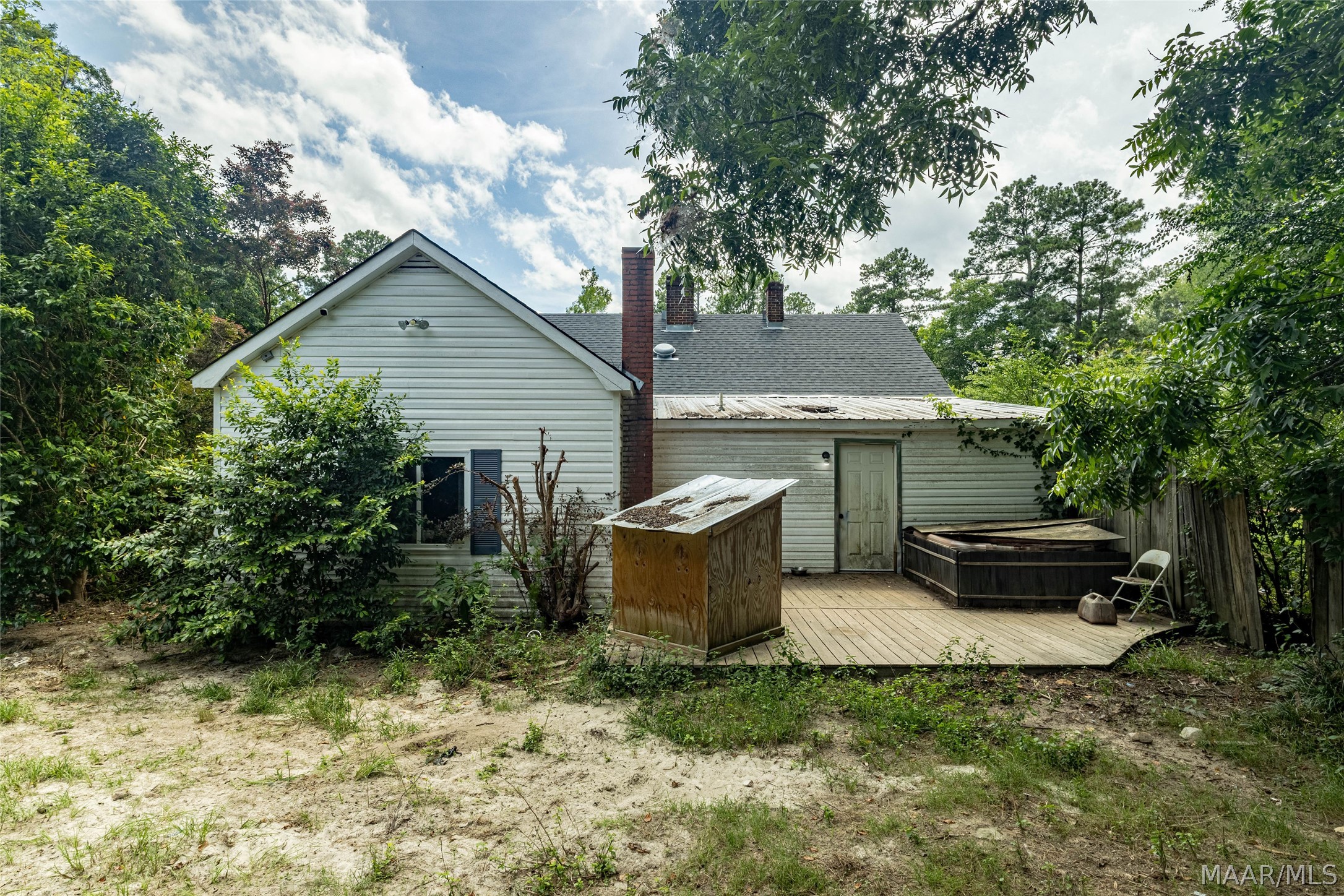Rear of a light-sided house with a wooden deck, hot tub, and tree-lined yard.