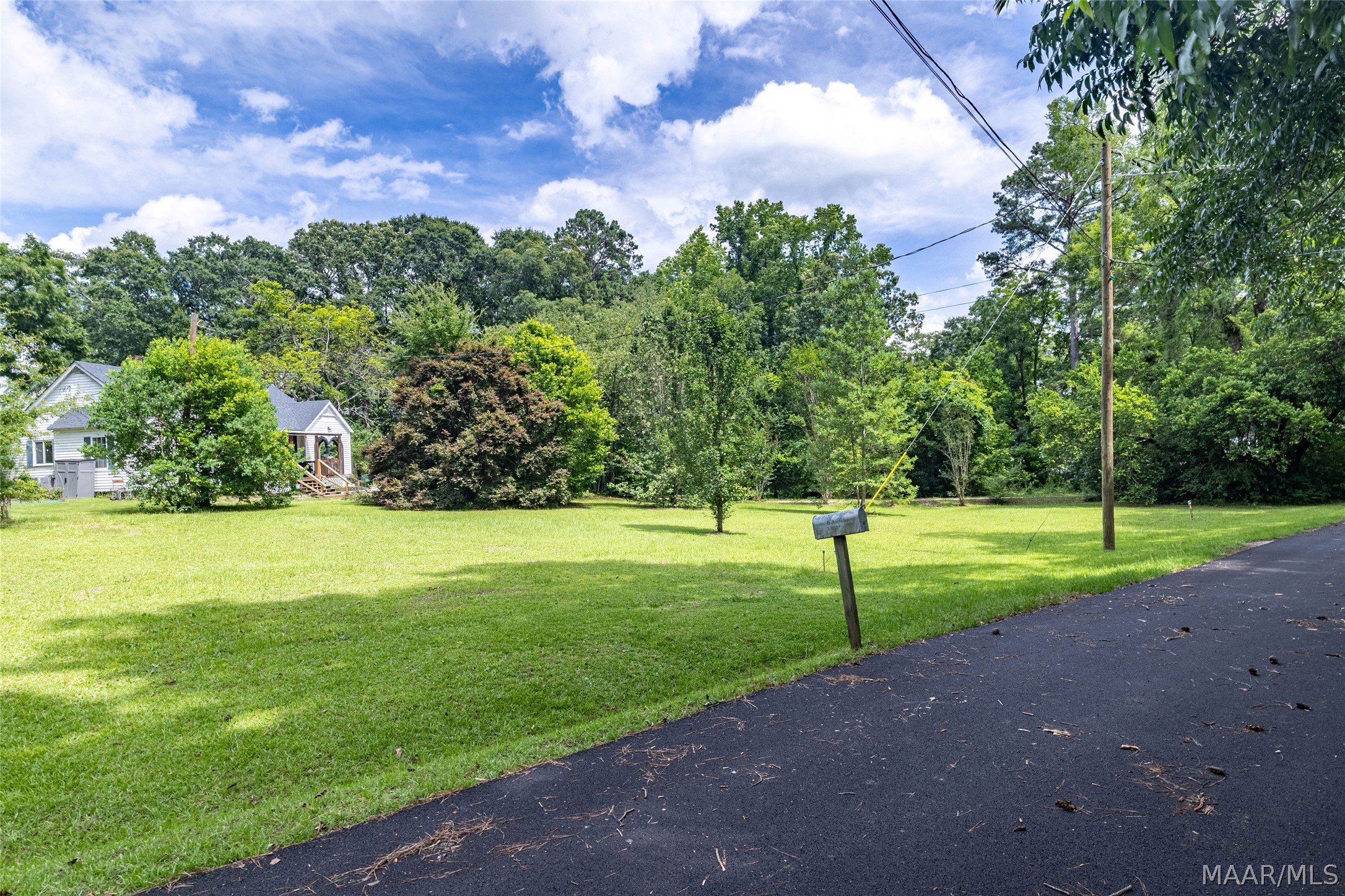 Property with a broad lawn, tree-screened house, and roadside mailbox.