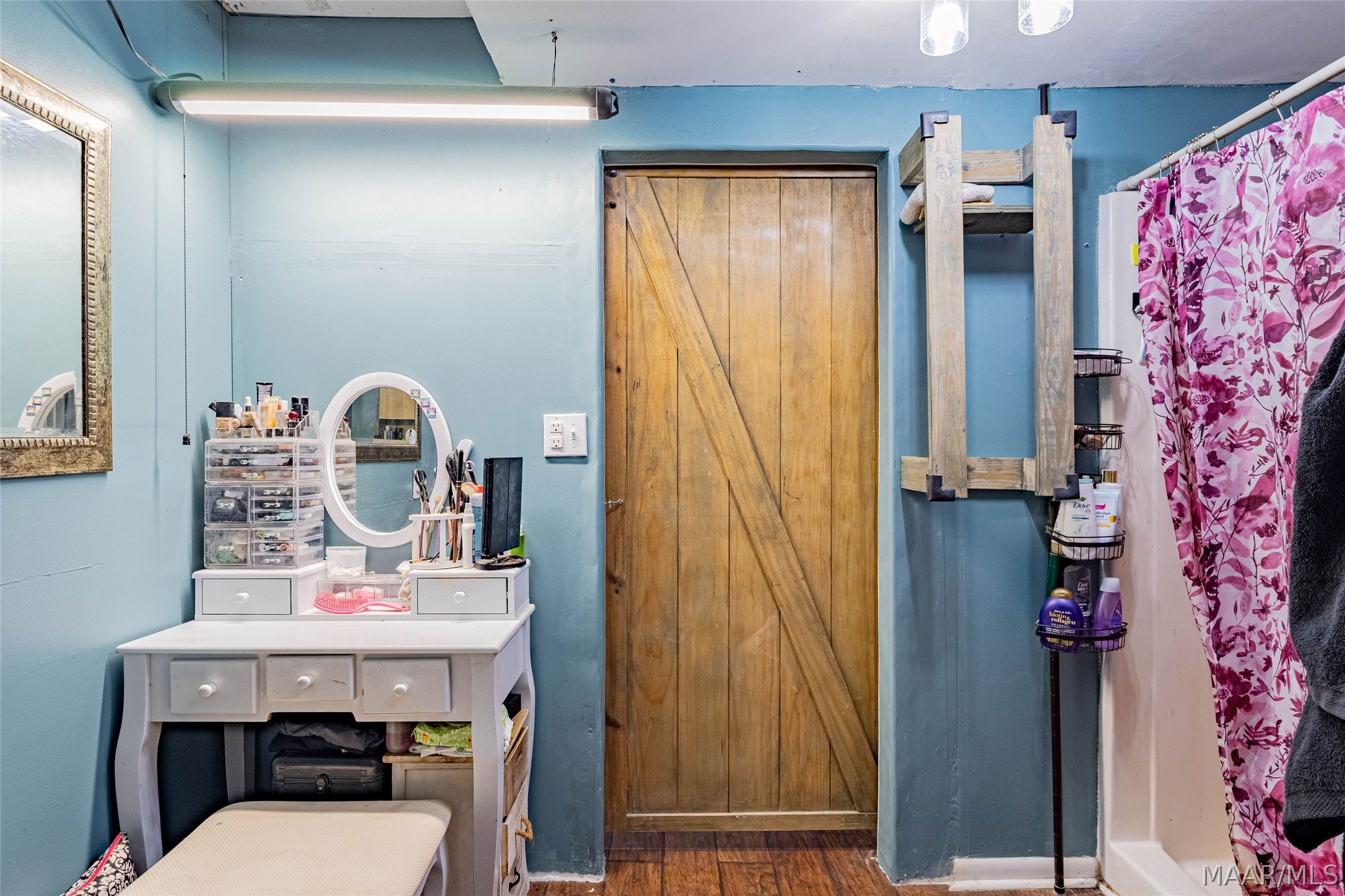 Bathroom with blue walls, a wooden barn-style door, and a white vanity beside a floral shower curtain.