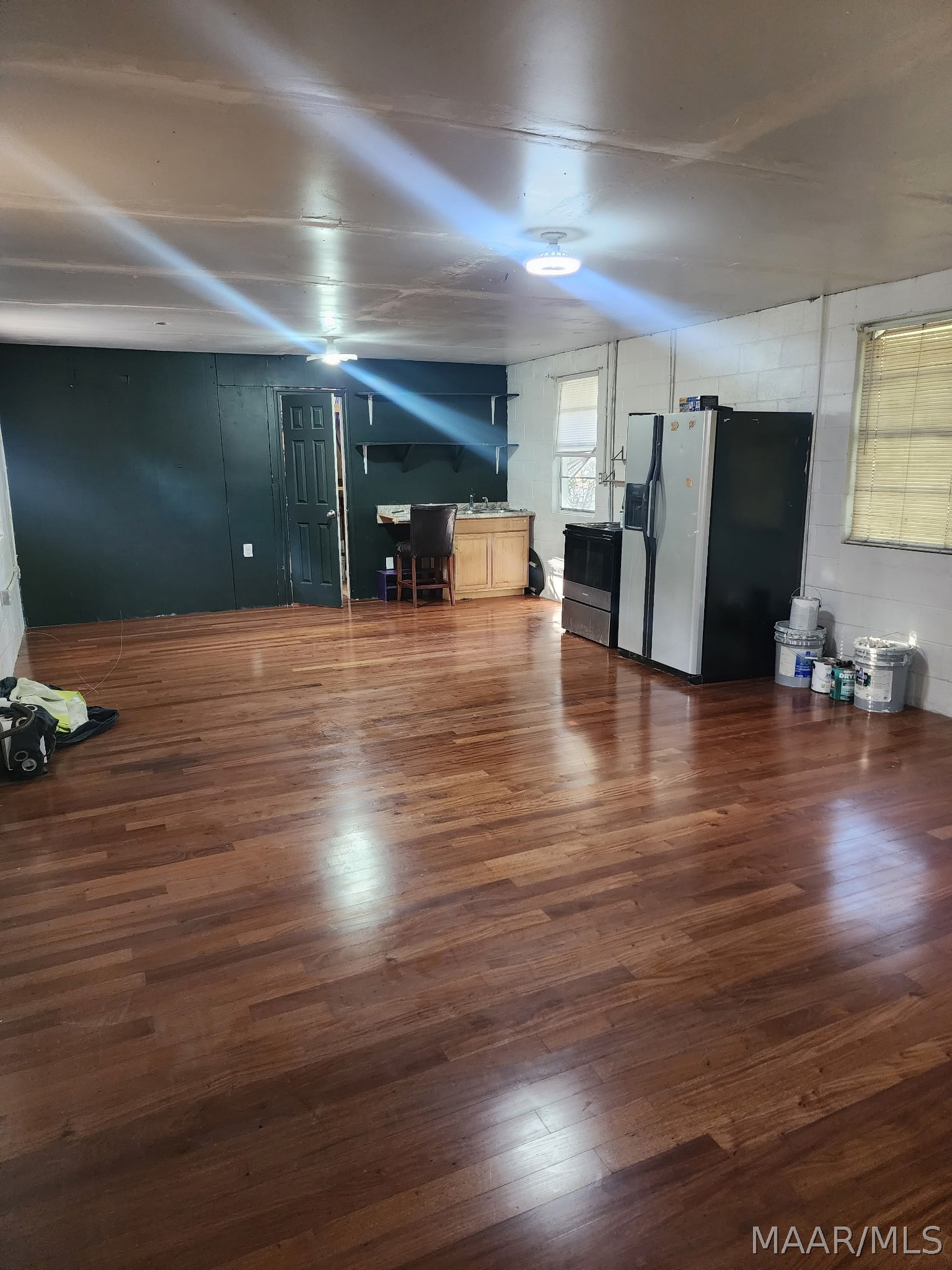 Open kitchen and living area with hardwood floors, dark green walls, and refrigerator and stove.