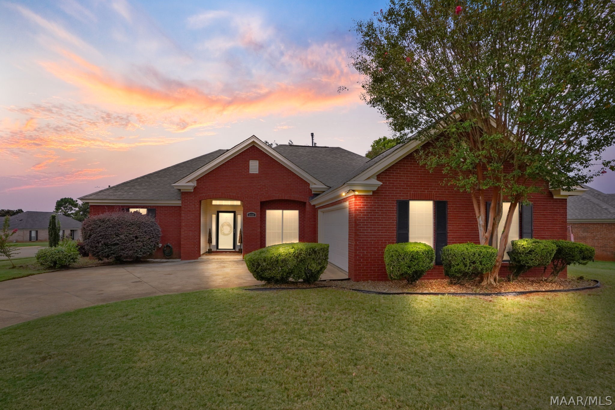 Red brick home with an attached garage and landscaped lawn beneath a colorful dusk sky.