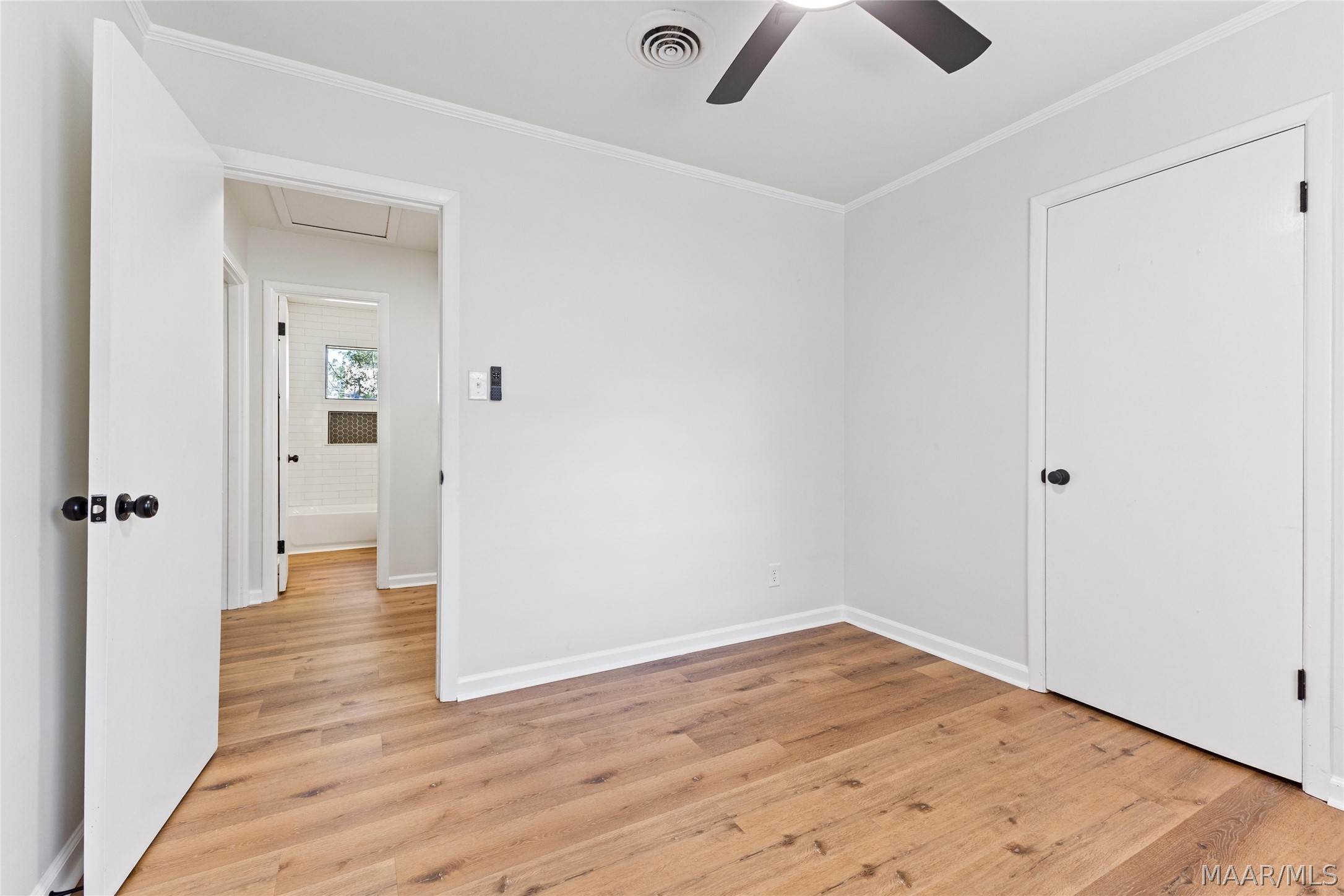 Vacant bedroom with warm wood floors, a ceiling fan, and an open doorway toward a tiled bathroom.