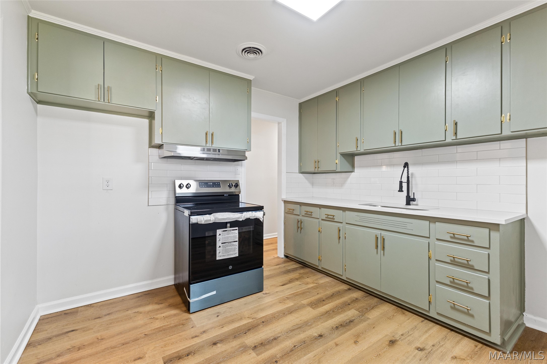 Kitchen with sage-green cabinets, brass hardware, white subway-tile backsplash, and a black range.
