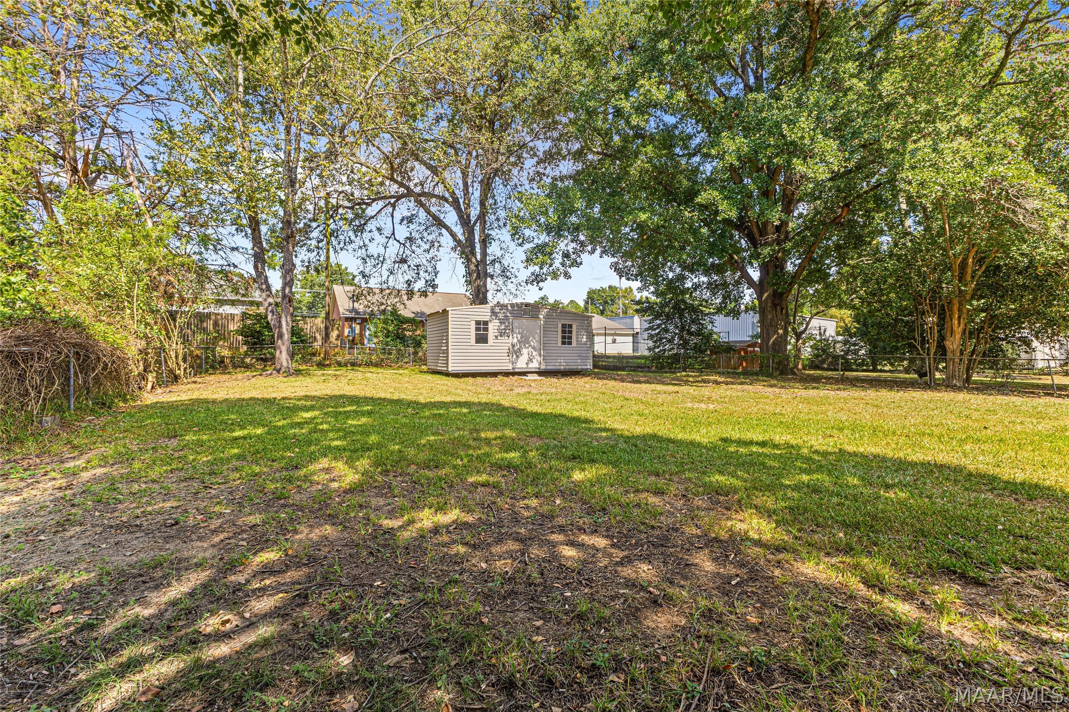 Spacious backyard with a detached shed beneath mature shade trees.
