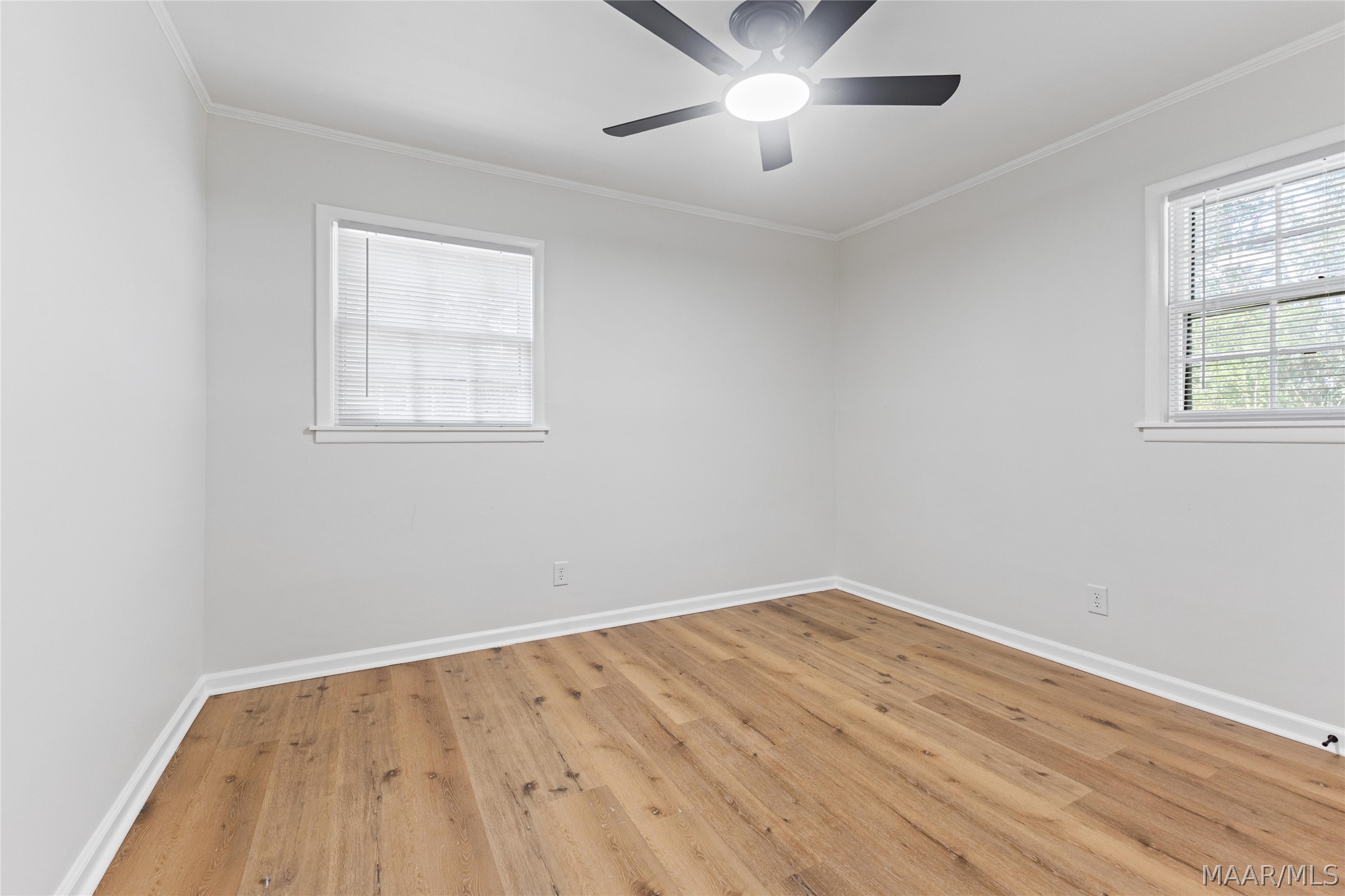 Vacant bedroom with two windows, wide-plank wood floors, and a ceiling fan.