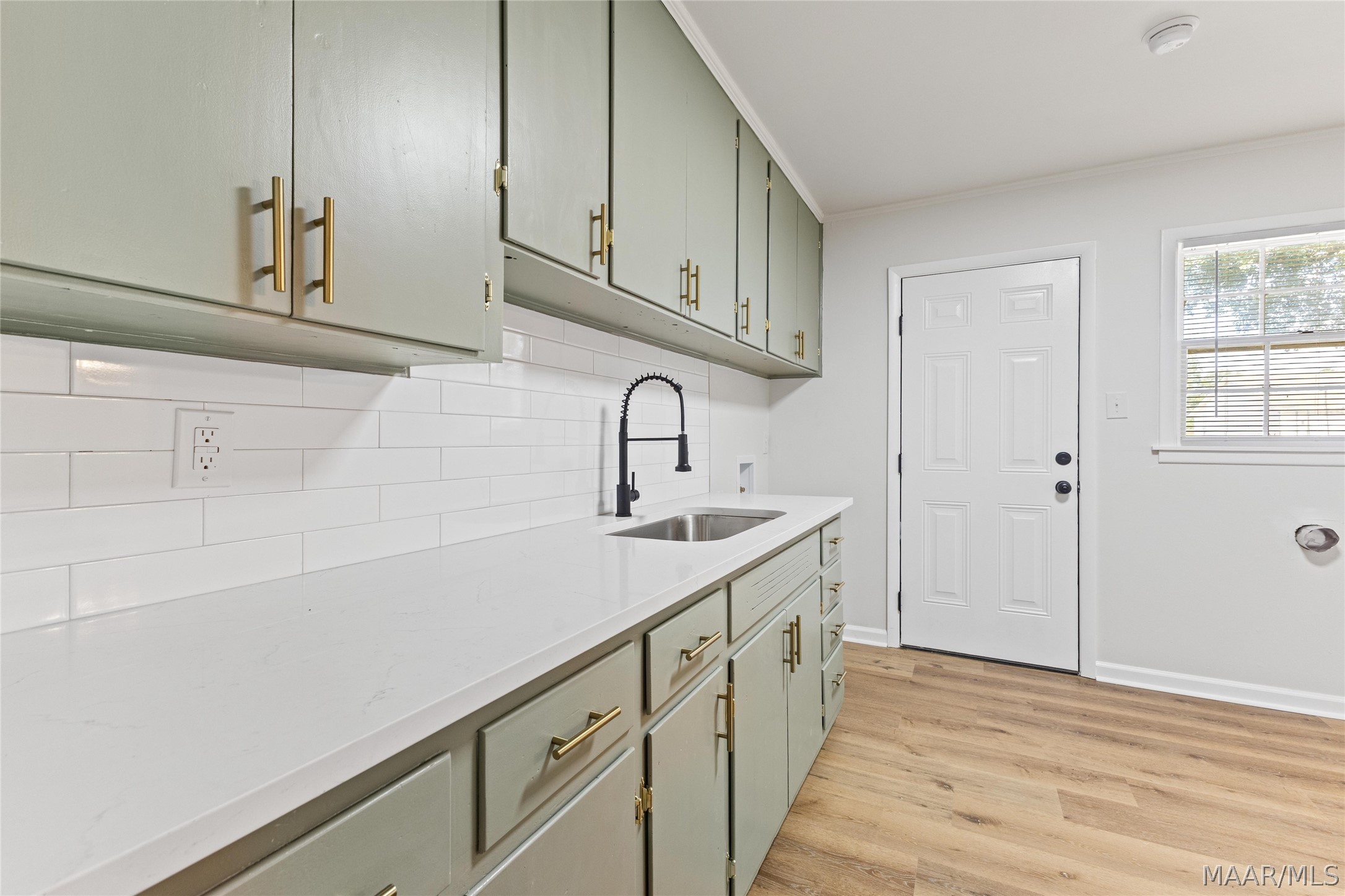 Kitchen with sage-green cabinets, white counters and tile backsplash, and a black spring-style faucet.