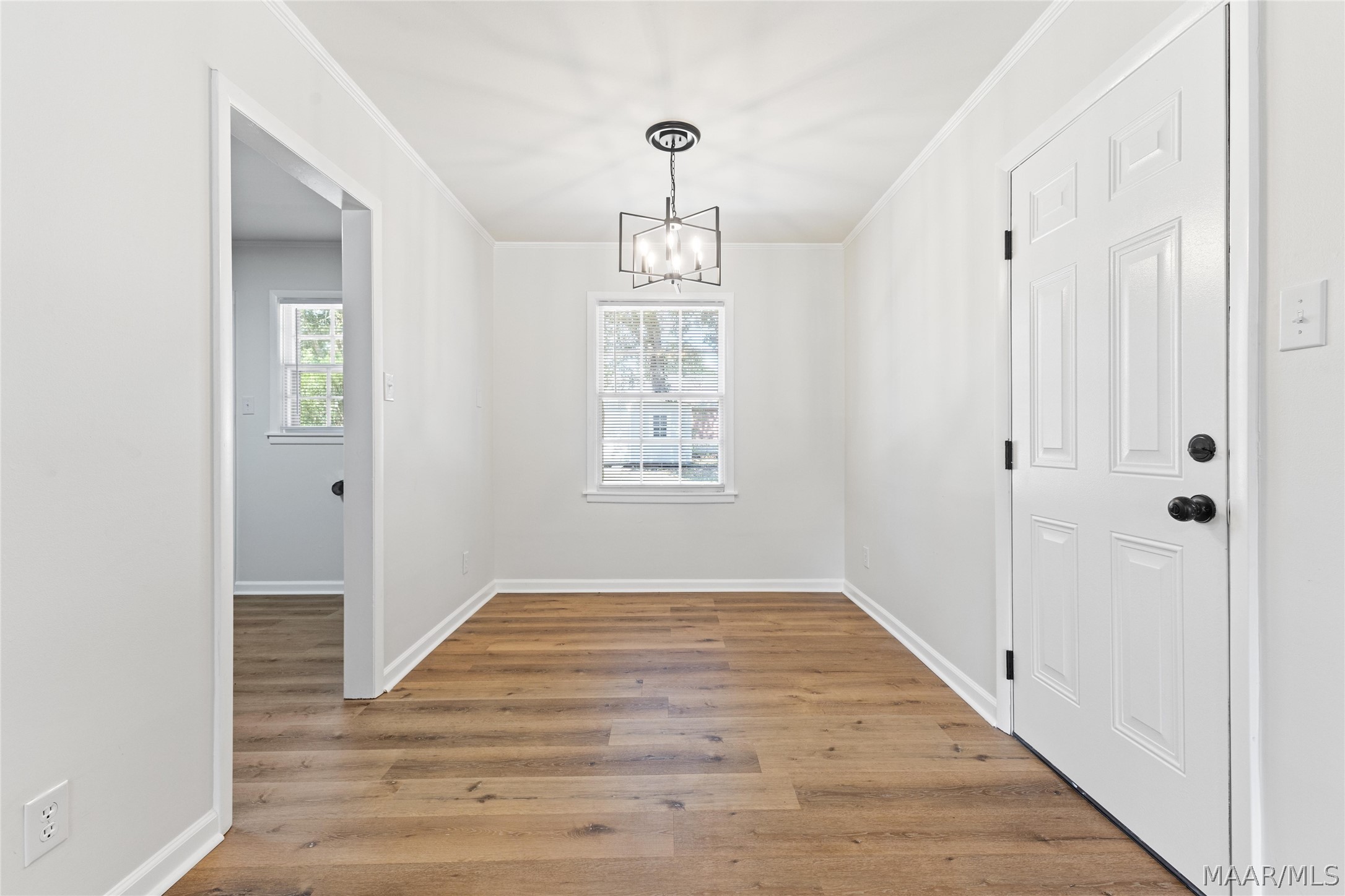 Empty dining area with wood-plank floors, a geometric chandelier, and a window with blinds.
