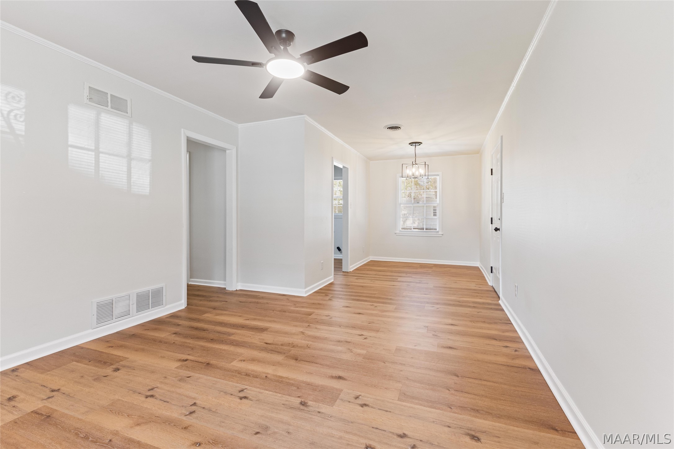 Vacant room with warm wood flooring, a ceiling fan, and a chandelier by a window.