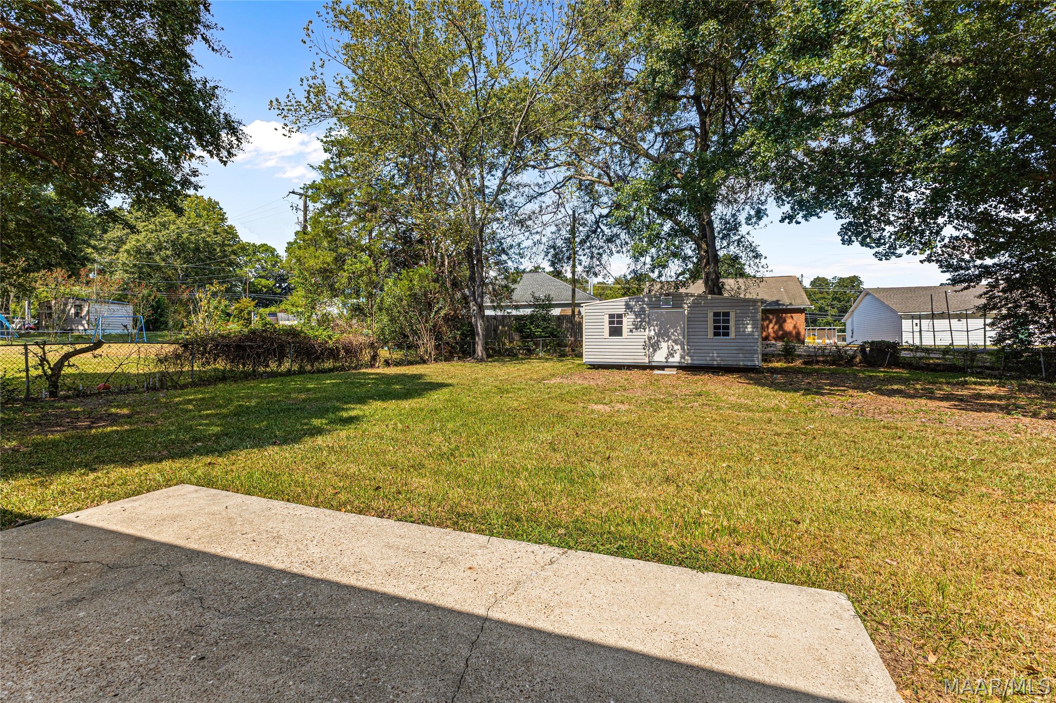 Backyard lawn with a concrete patio, mature trees, and a detached storage shed.