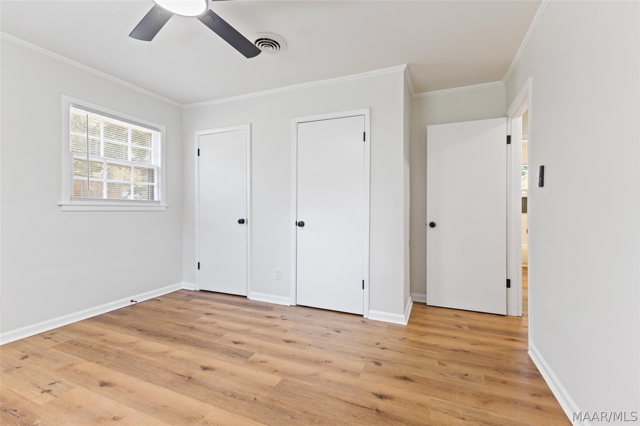 Vacant room with wood flooring, a ceiling fan, and several white doors.