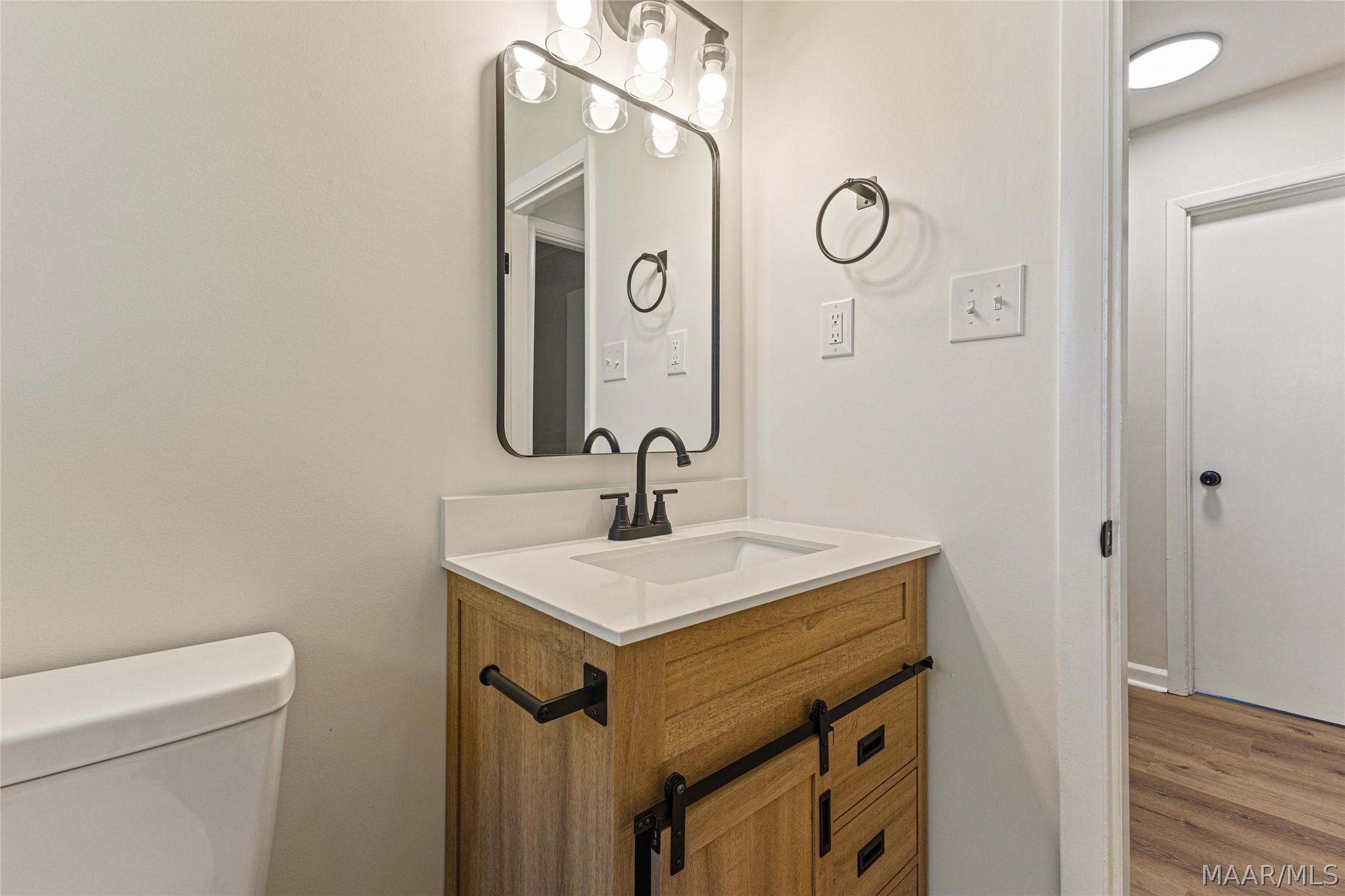 Bathroom with a wood vanity, barn-door hardware, black faucet, and illuminated mirror.