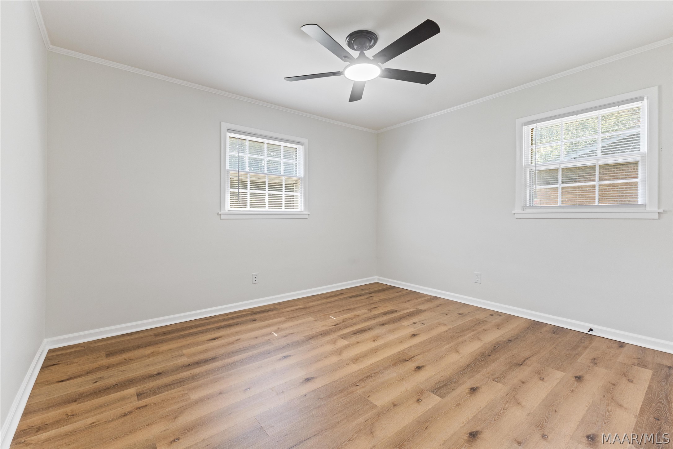 Empty bedroom with wood-look floors, two windows, and a dark ceiling fan.
