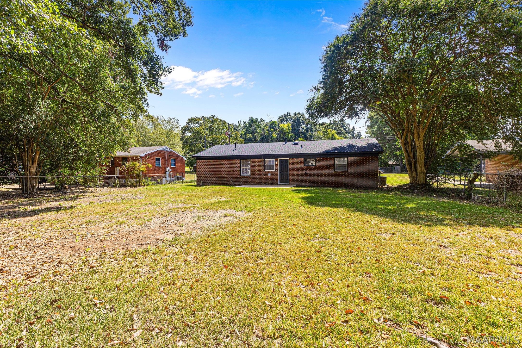 Rear of a single-story brick house across a broad grassy yard framed by mature trees.
