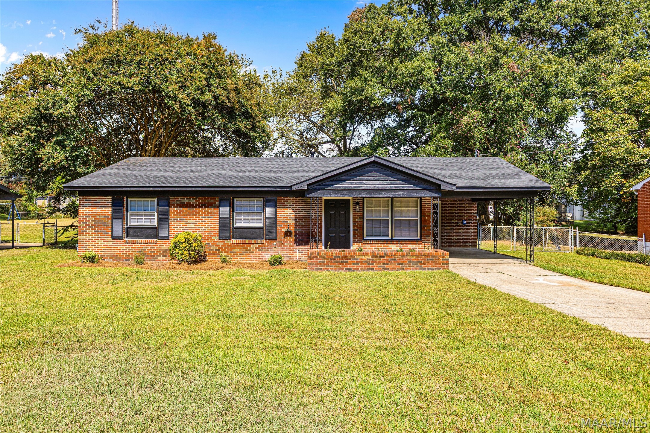 Single-story brick ranch with a covered entry, side carport, broad lawn, and mature trees.