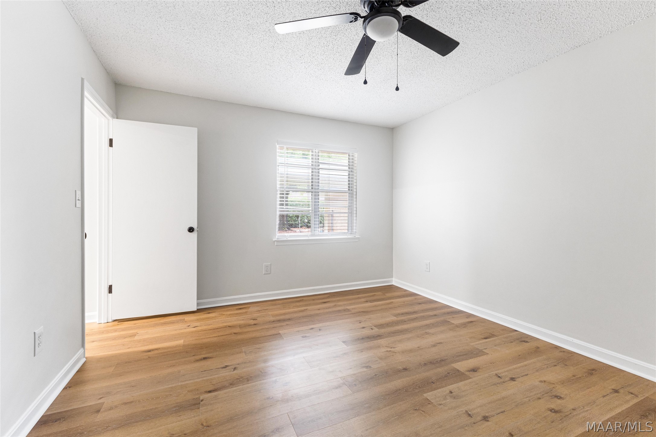 Empty room with wood-look flooring, a window with blinds, and a black ceiling fan.