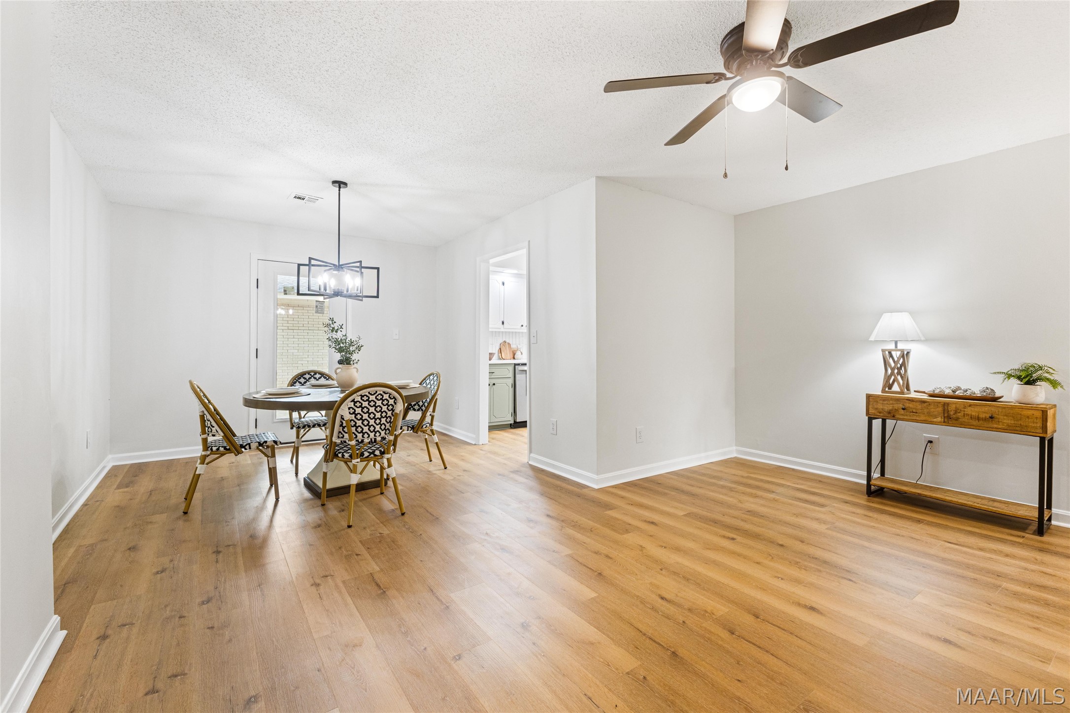 Dining area with a round table, patterned chairs, wood flooring, and a doorway to the kitchen.