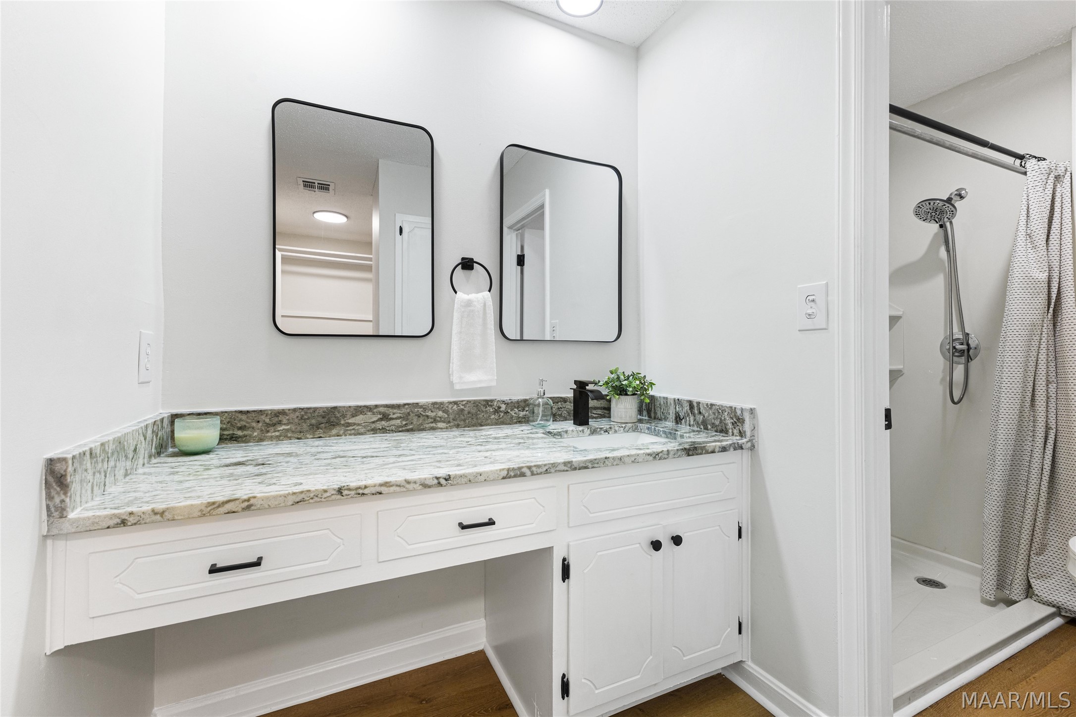 Bathroom vanity with veined stone countertop, twin mirrors, and an adjoining walk-in shower.