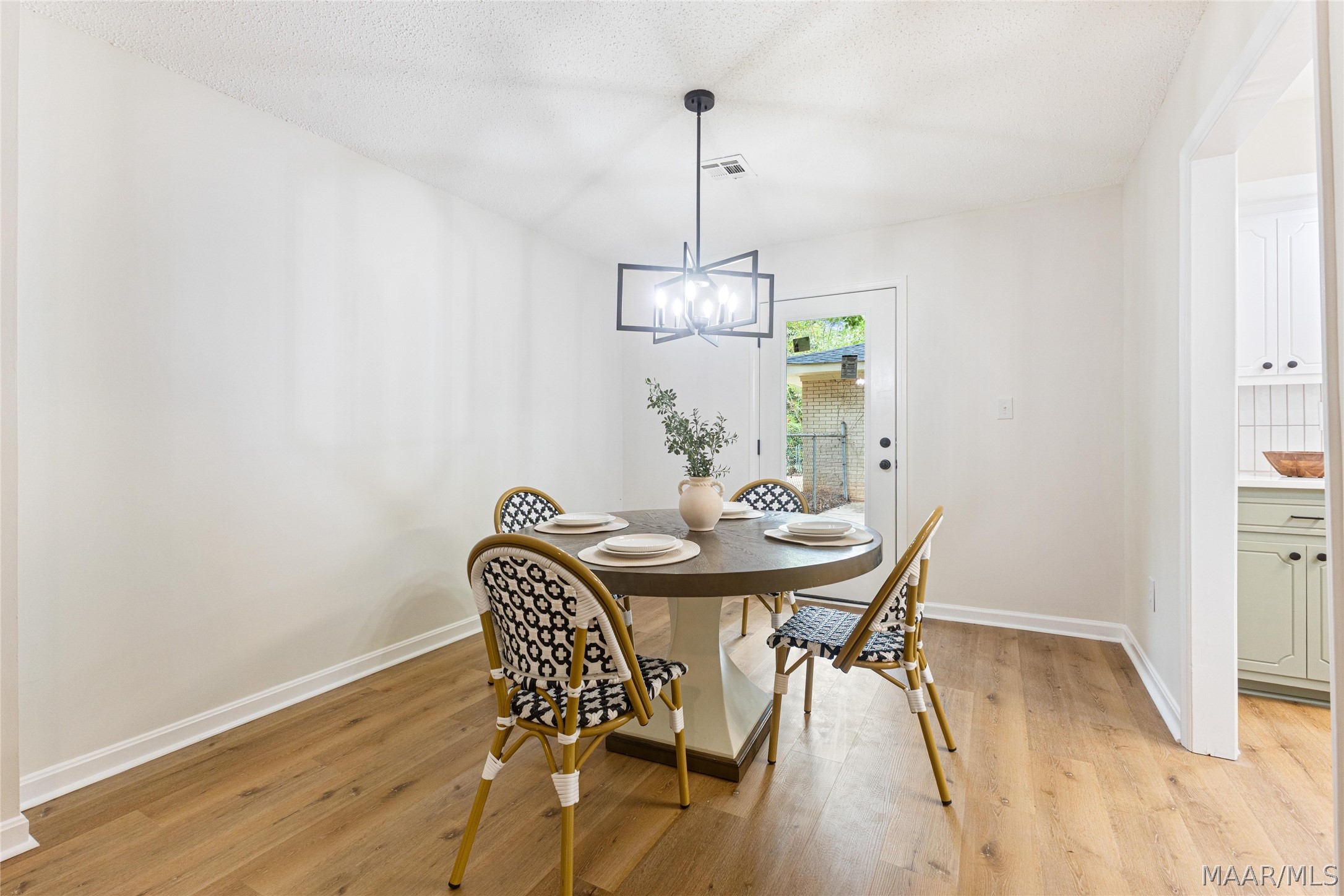 Dining room with a set round table, patterned chairs, geometric pendant light, and wood-look flooring.