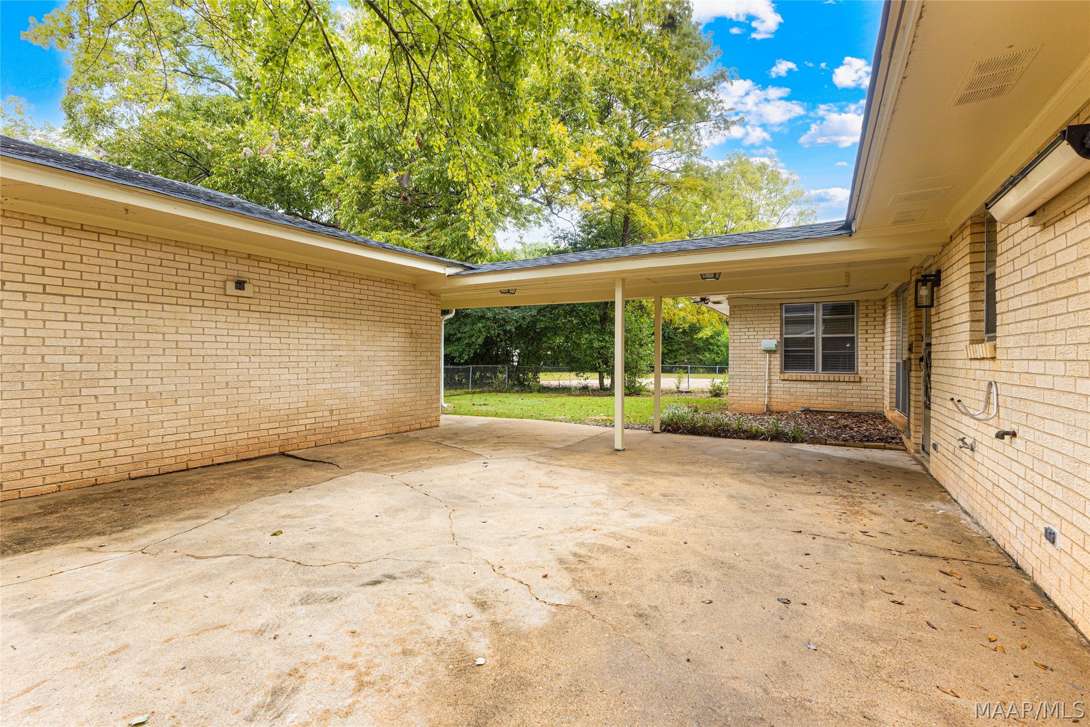 Covered concrete patio beside a brick home, opening onto a fenced yard.