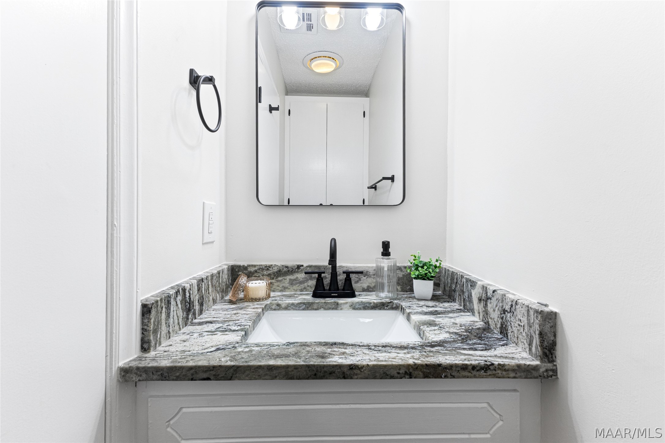 Bathroom vanity with a gray stone counter, white sink, black faucet, and rectangular mirror.