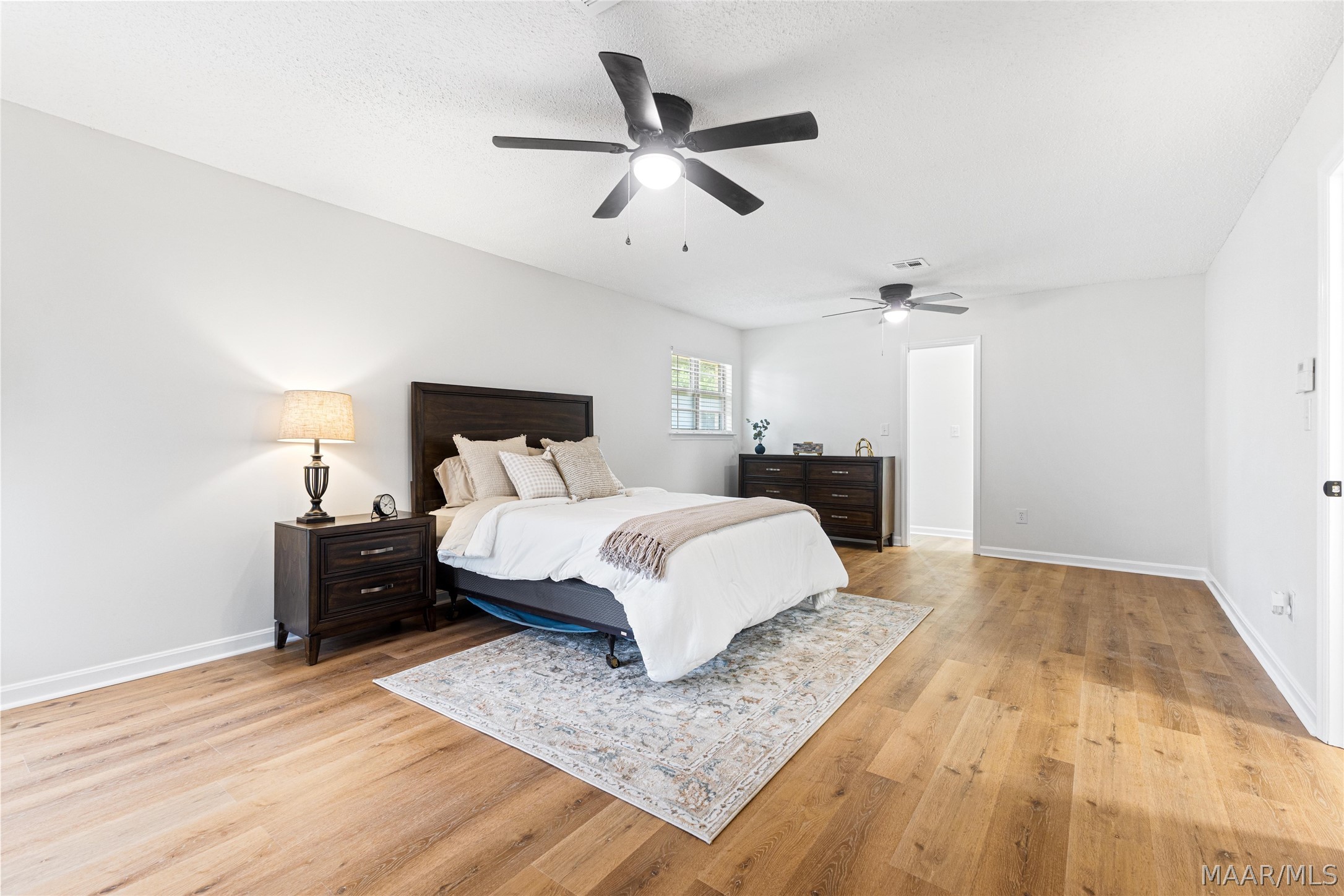 Furnished bedroom with dark wood furniture, white bedding, two ceiling fans, and warm wood floors.