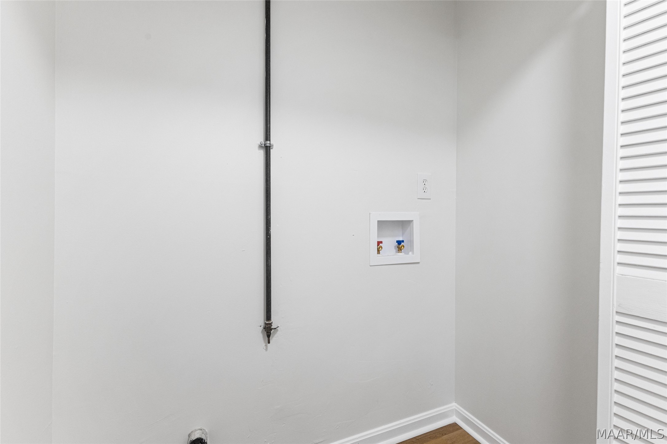 Empty laundry area with washer and dryer hookups beside a louvered closet door.
