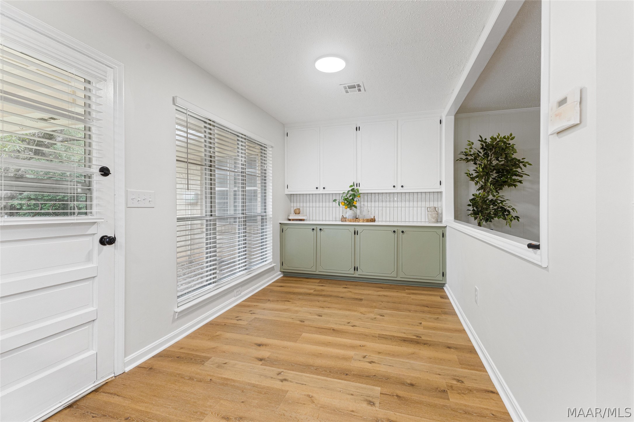 Kitchen with sage-green lower cabinets, white upper cabinets, and warm wood floors.