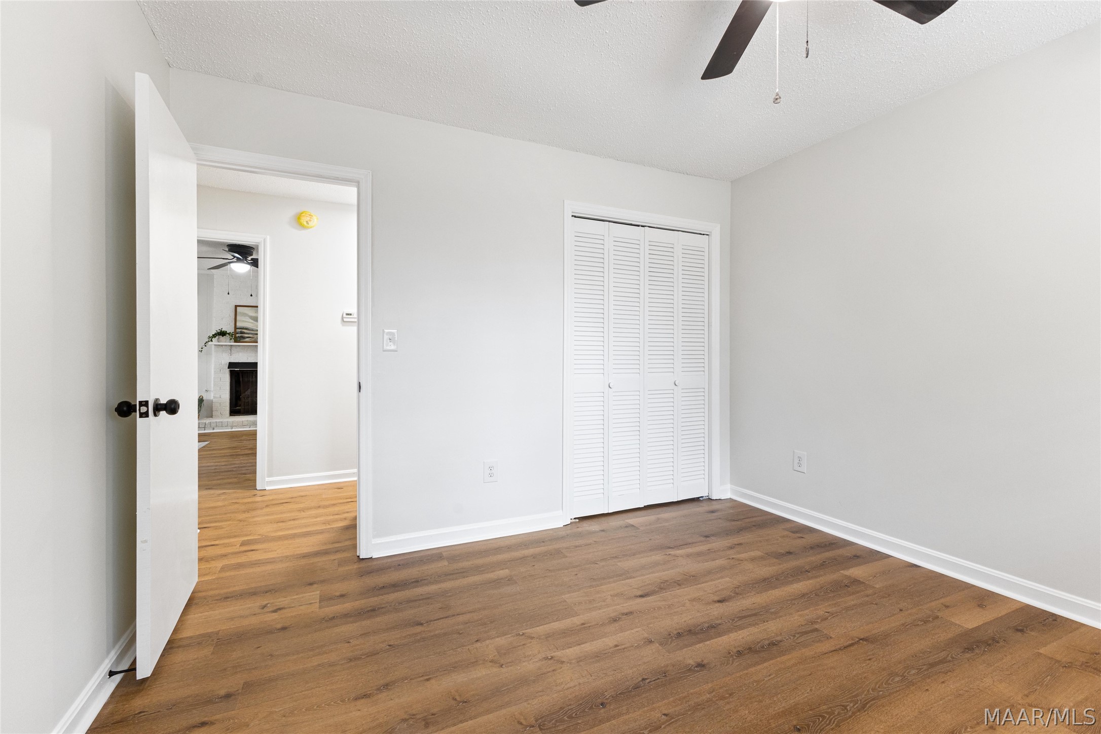 Empty bedroom with wood floors, a ceiling fan, and a louvered closet.