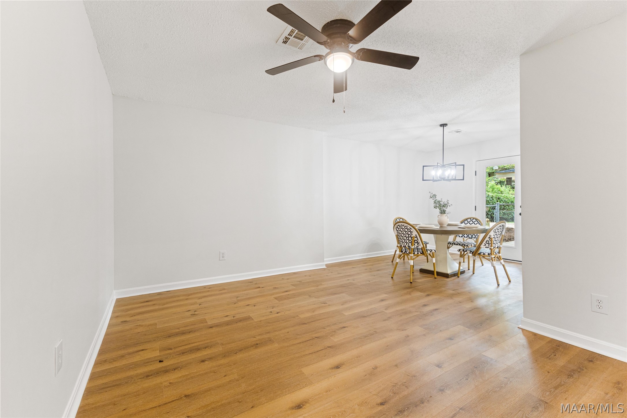 Dining area with wood plank floors, a round table, patterned chairs, and a glass door to greenery.