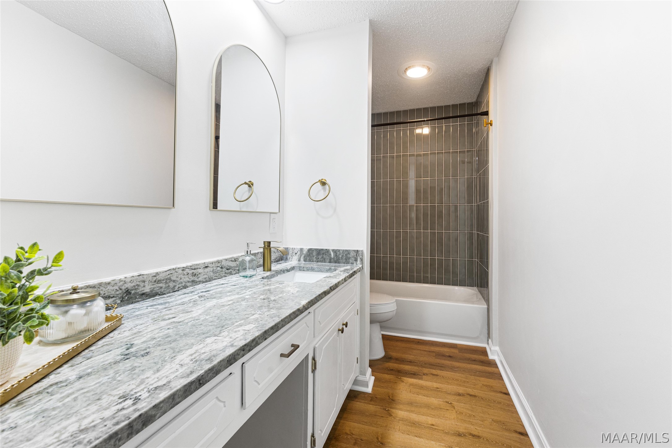Bathroom with a veined stone vanity, brass fixtures, and a dark gray tiled tub-shower.
