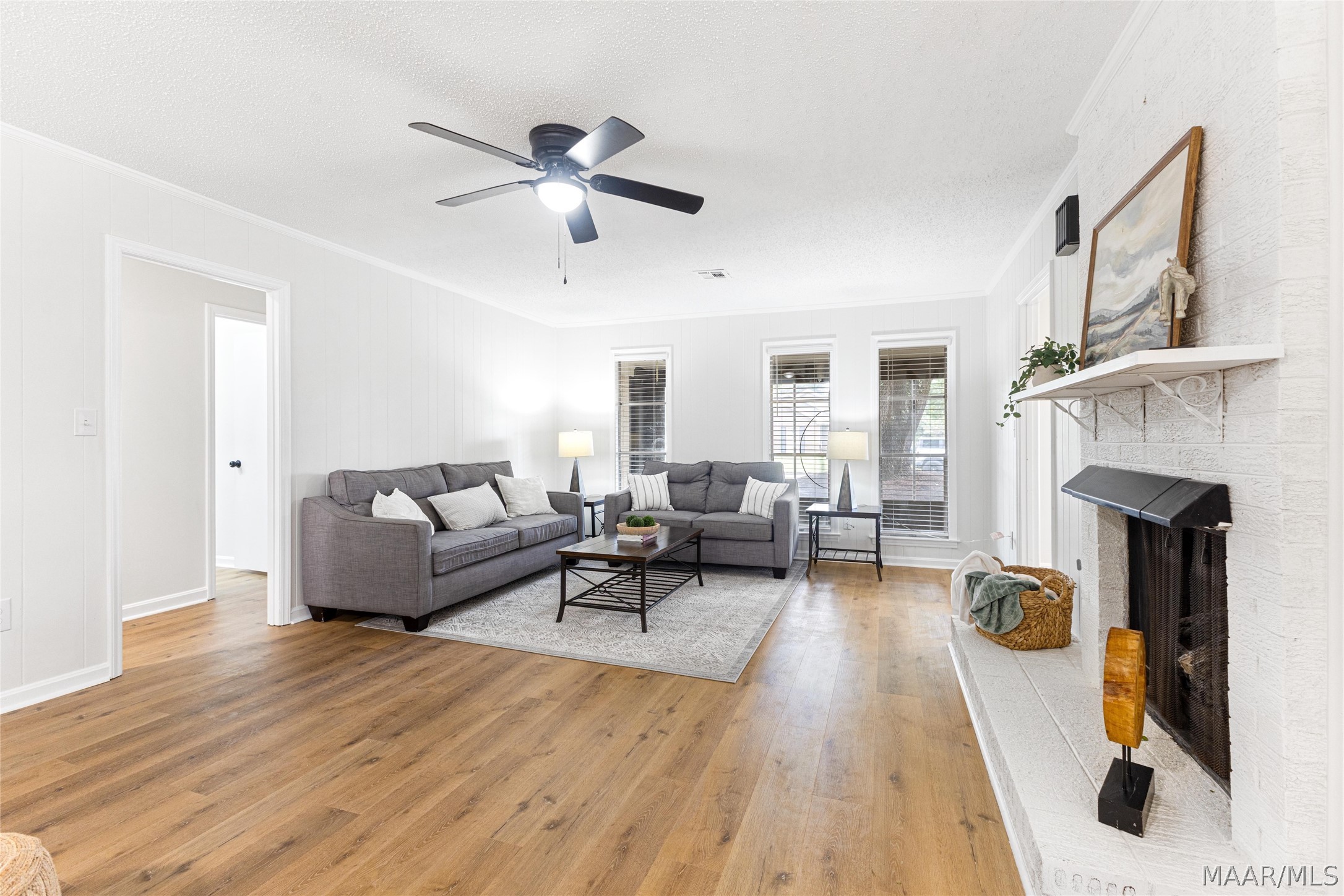 Living room with gray sofas, wood floors, and a white brick fireplace.