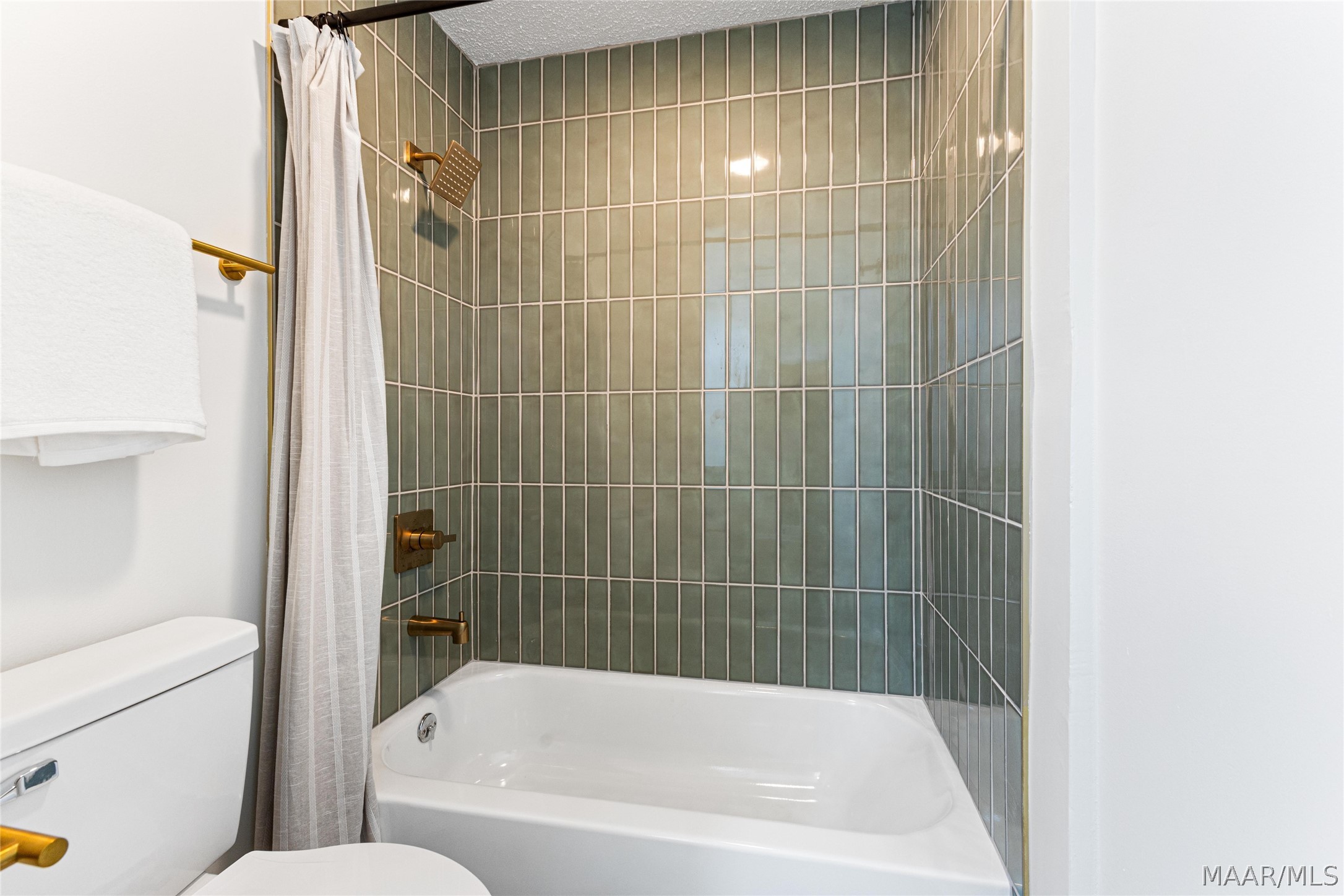 Bathroom bathtub and shower with green-gray tile, white curtain, and brass fixtures.