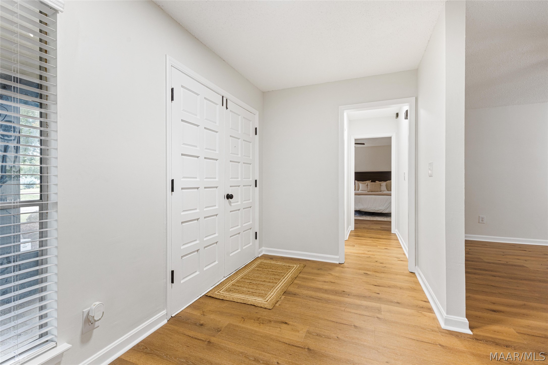 Hallway with white paneled closet doors, wood floors, and a view into a bedroom.