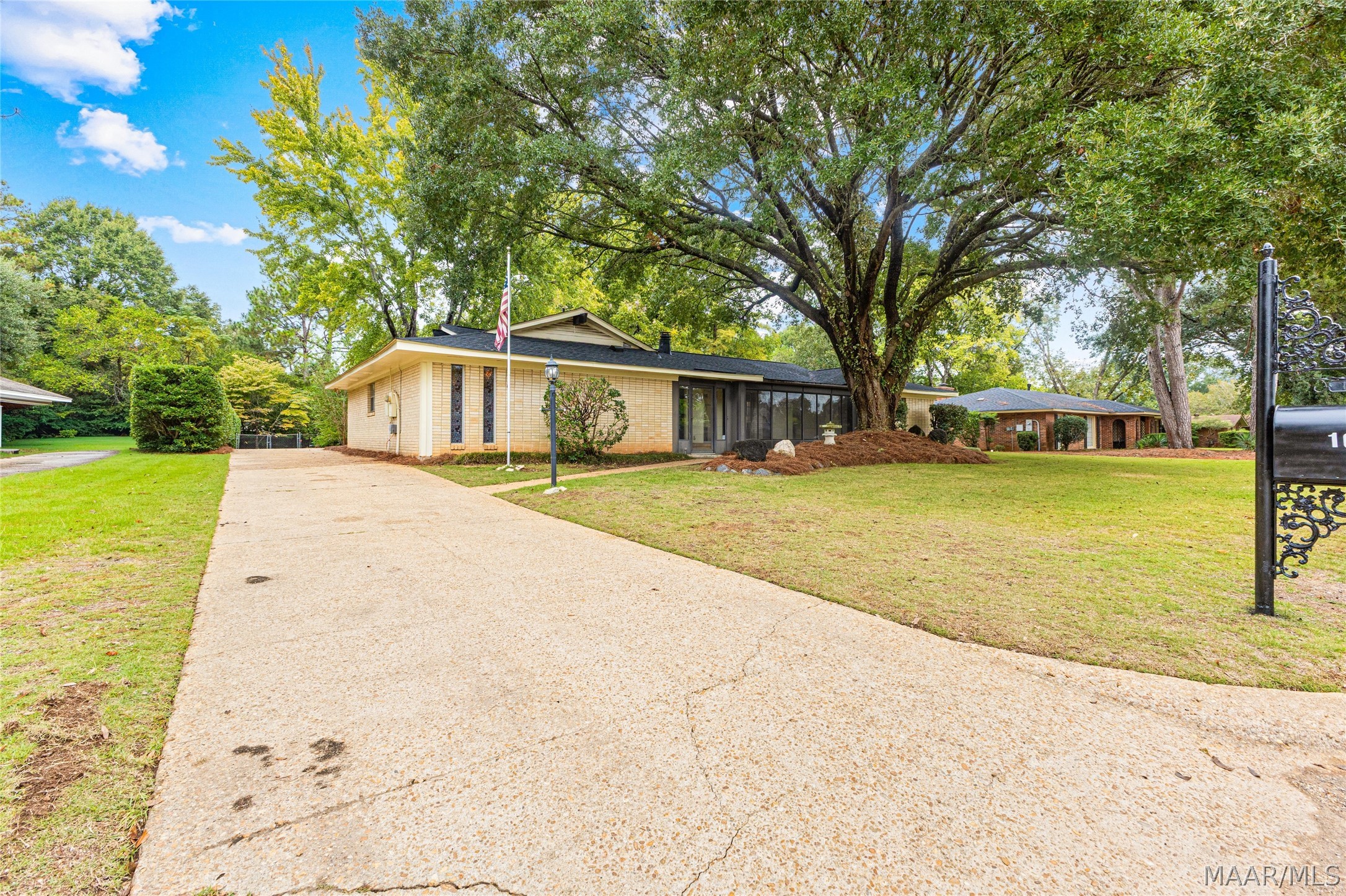 Single-story brick home with a screened porch, broad driveway, and large shade tree.