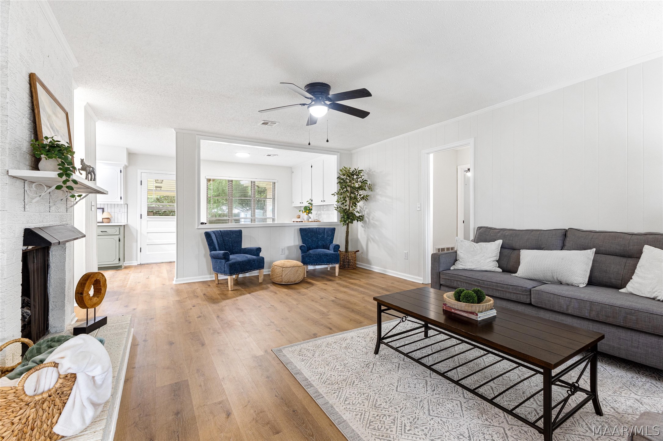 Furnished living room with a gray sofa, blue armchairs, and a white brick fireplace.