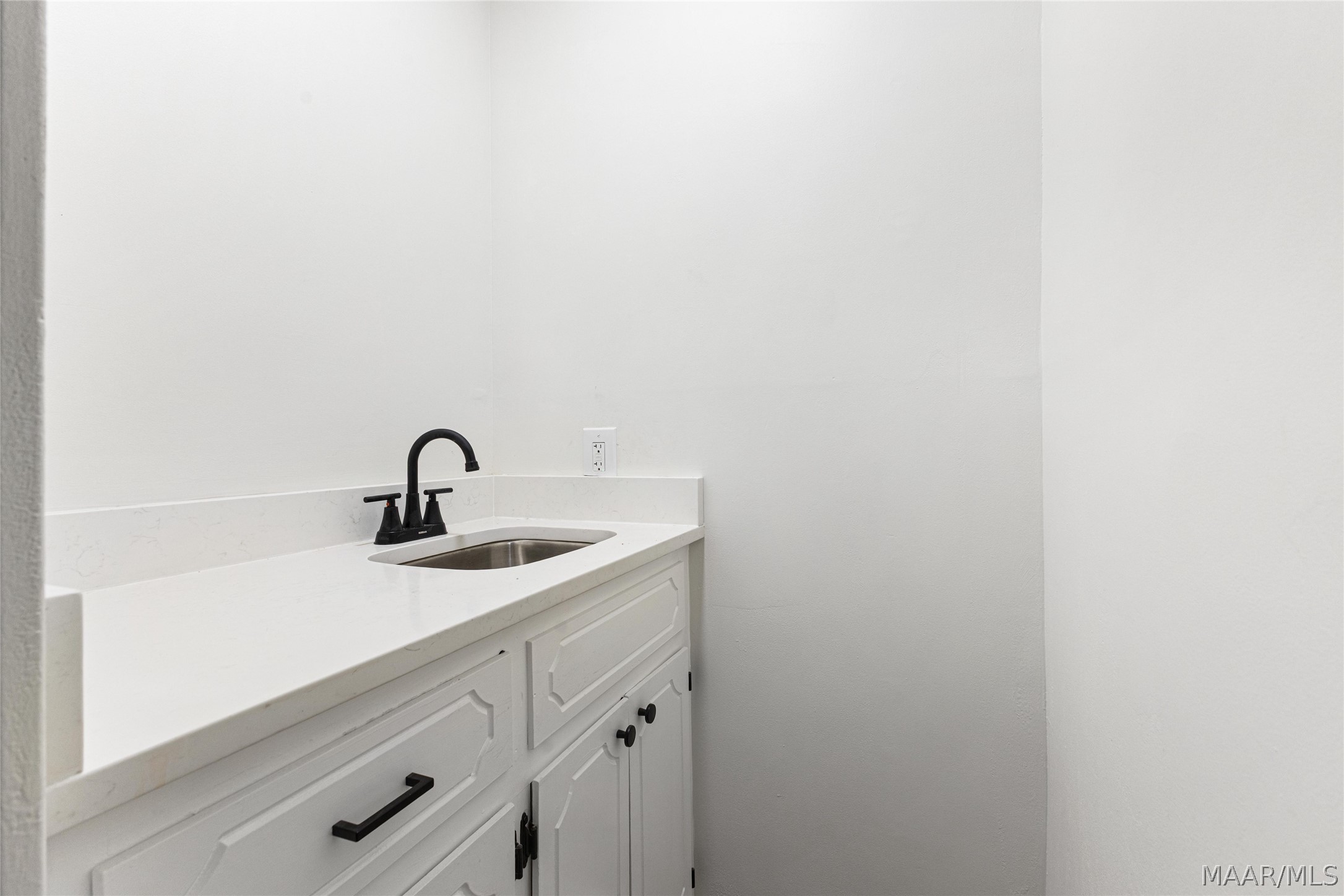 White bathroom vanity with an inset sink, black faucet, and paneled cabinets.