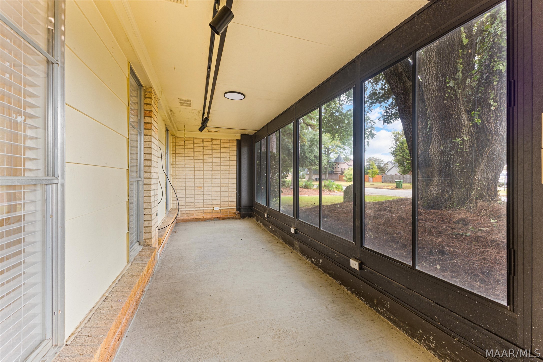 Enclosed sunroom with a concrete floor and large windows overlooking a mature tree.