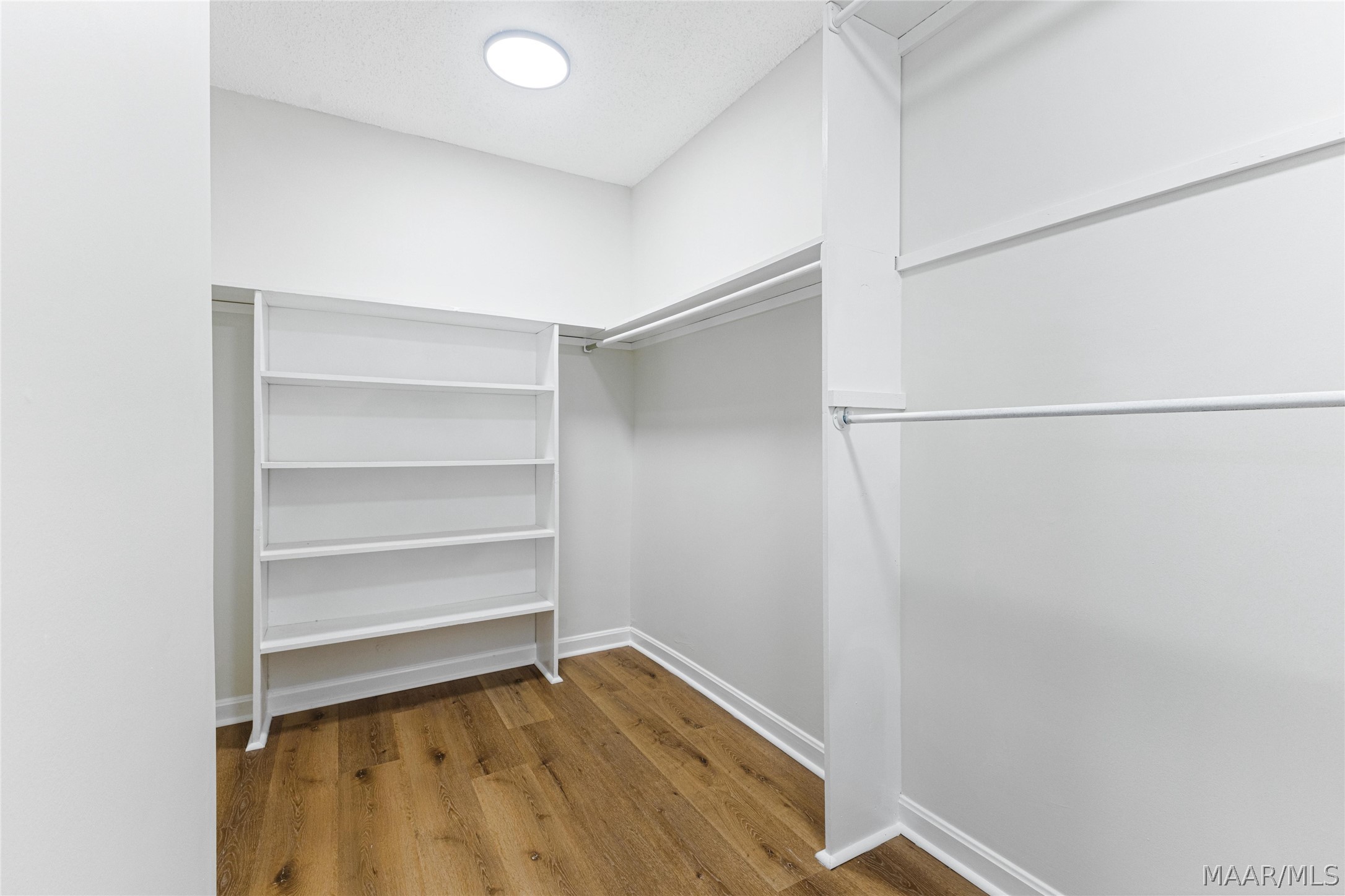 Walk-in closet with built-in white shelving, hanging rods, and wood flooring.