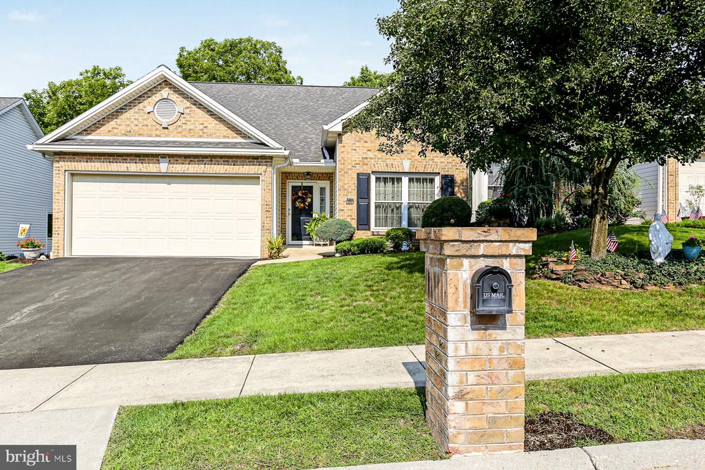 Brick home with a white double garage door, landscaped lawn, and a brick mailbox pillar by the sidewalk.