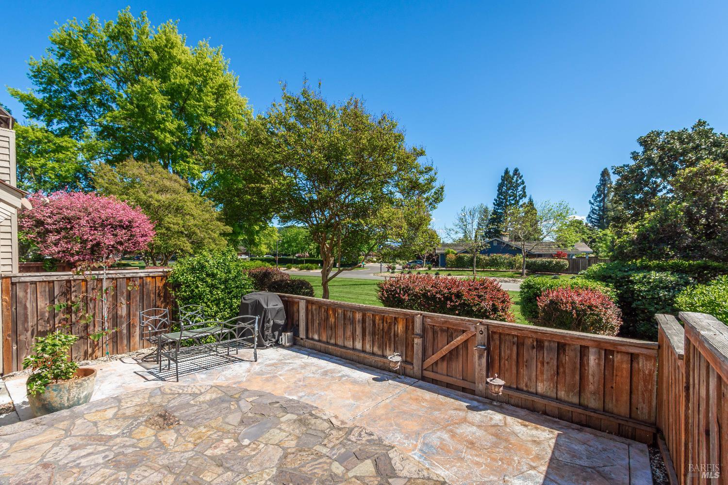 Flagstone patio with metal seating overlooking a fenced, landscaped yard with flowering shrubs and mature trees.
