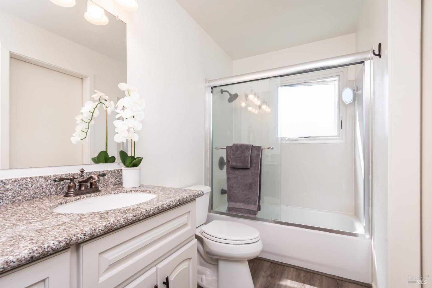 Bathroom with a granite vanity and white orchids beside a glass-enclosed tub and shower.