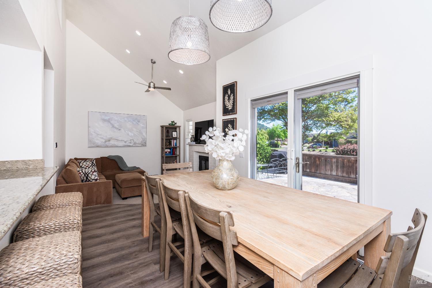 Open-plan living and dining room with a long wood table, vaulted ceiling, and sliding doors to the patio.