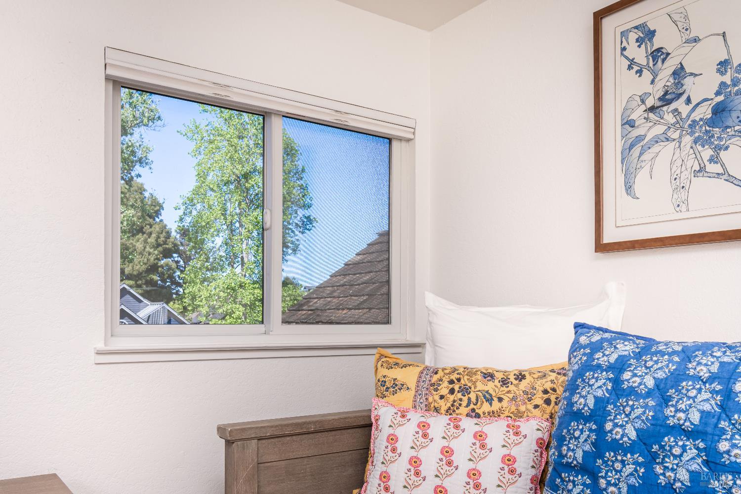 Bedroom with a sliding window, colorful floral pillows, and blue botanical wall art.