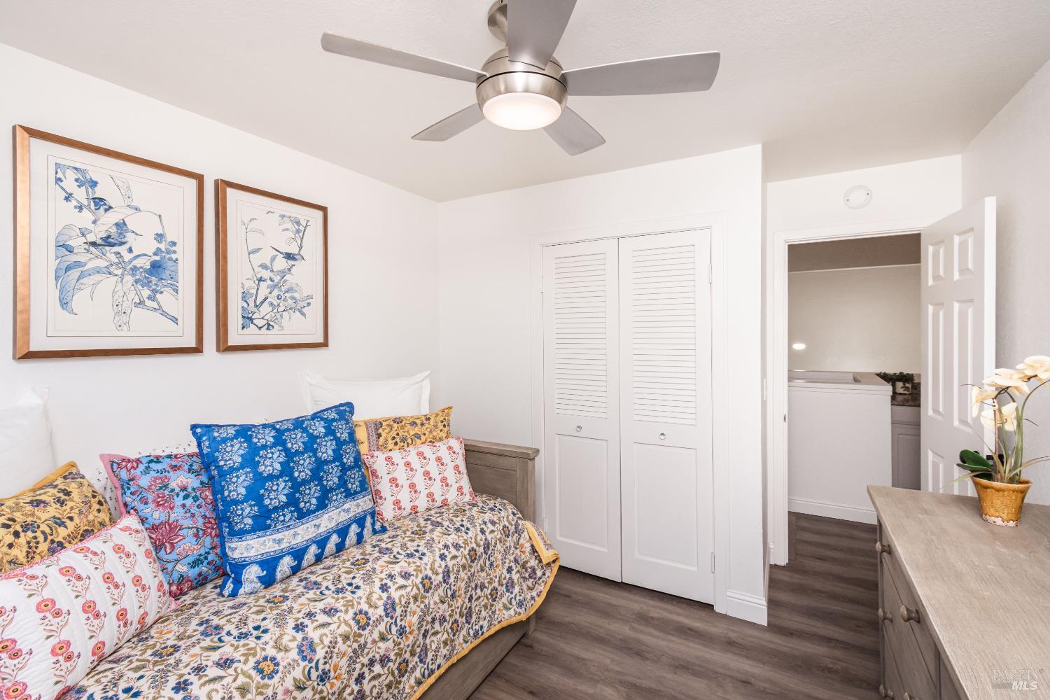 Bedroom with colorful floral bedding, framed botanical prints, and an open doorway to the laundry area.