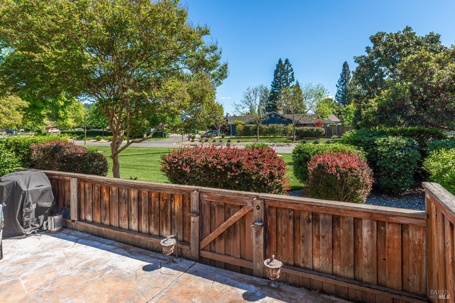Patio with stamped concrete and wooden fence overlooking a landscaped lawn and tree-lined residential street.