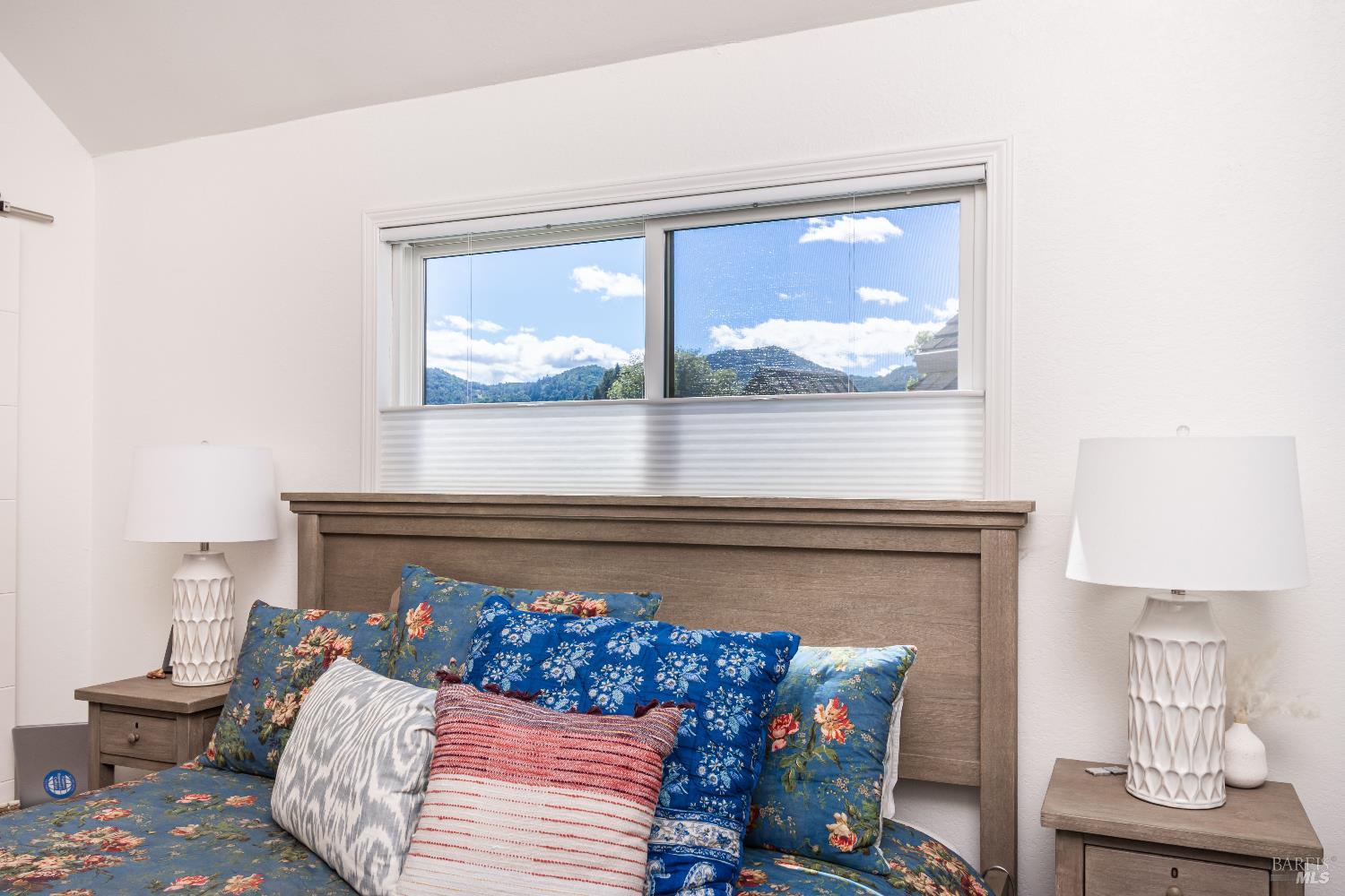 Bedroom with colorful floral bedding, wooden headboard, and a window overlooking green hills.
