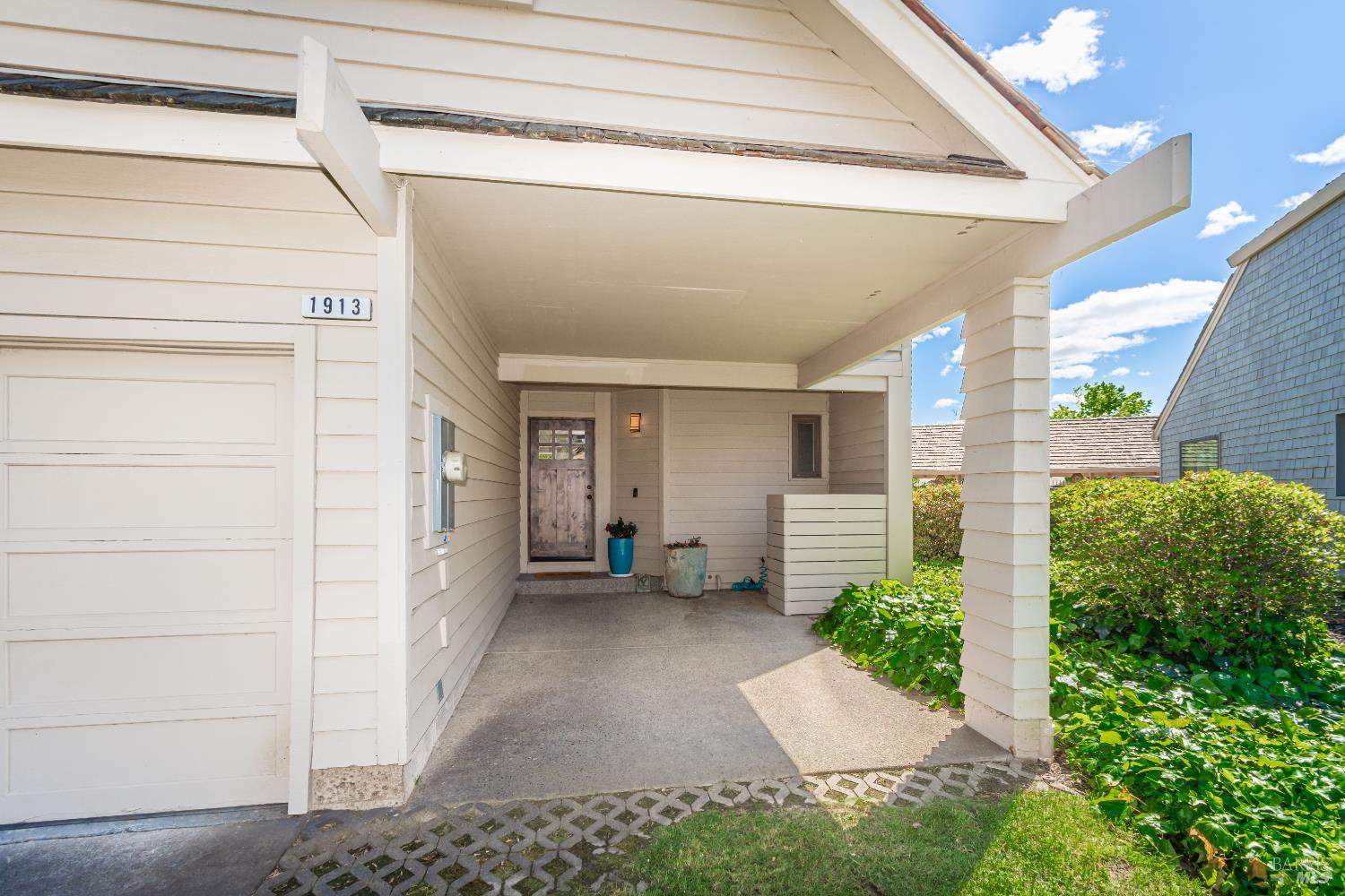 Covered entrance and garage at 1913 Hopper Way, with a weathered front door and leafy landscaping.
