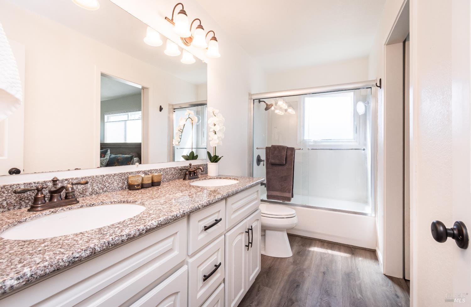 Bathroom with a double-sink vanity, speckled countertop, and windowed tub-shower.